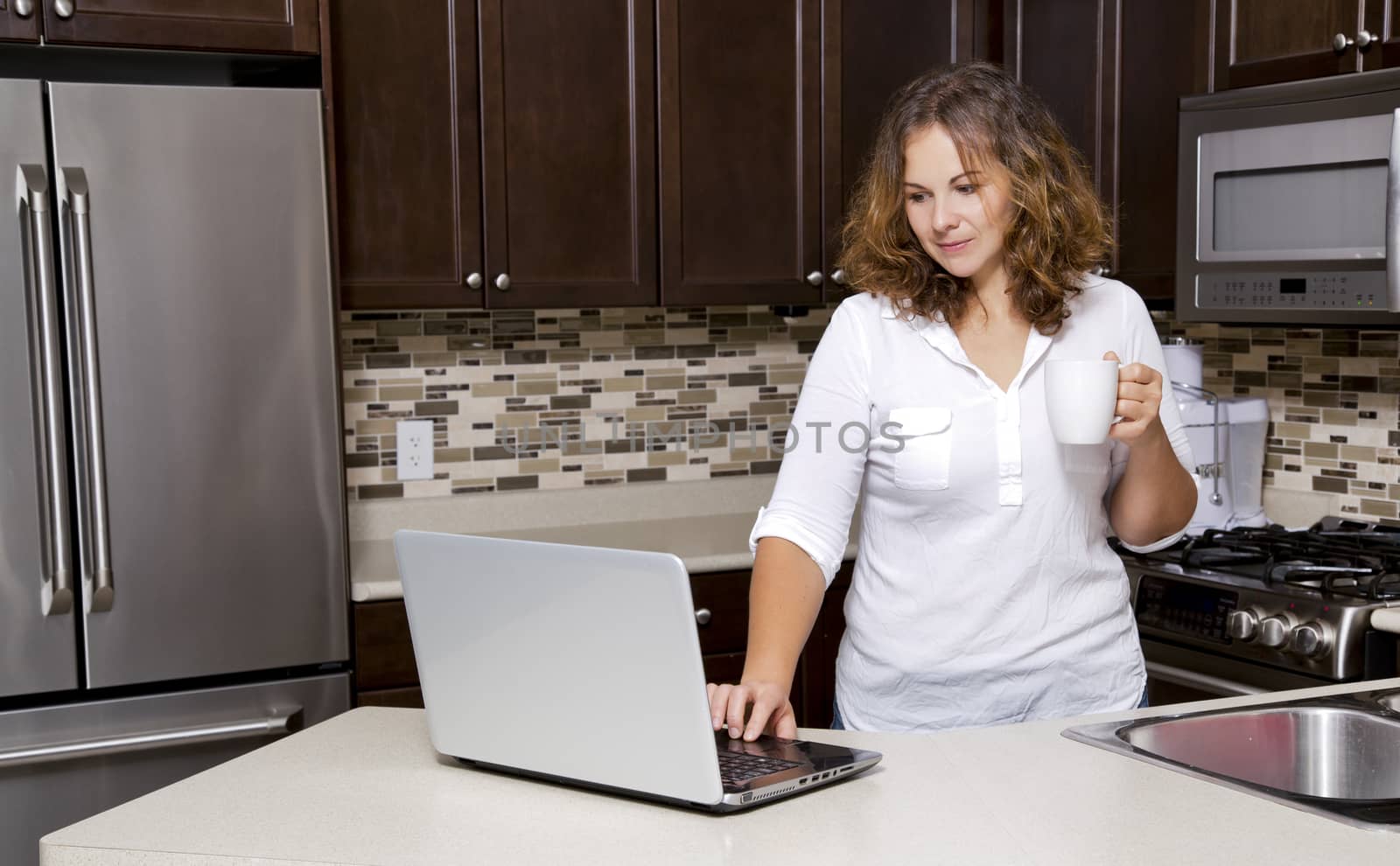 woman drinking coffee while working on the laptop in the kitchen