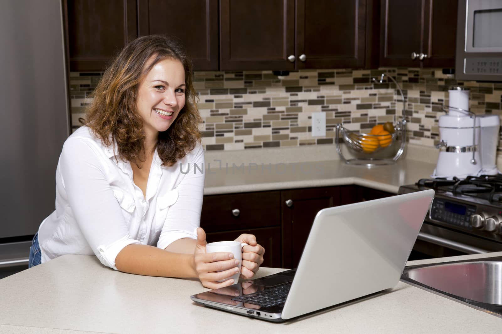 woman drinking coffee while working on the laptop in the kitchen