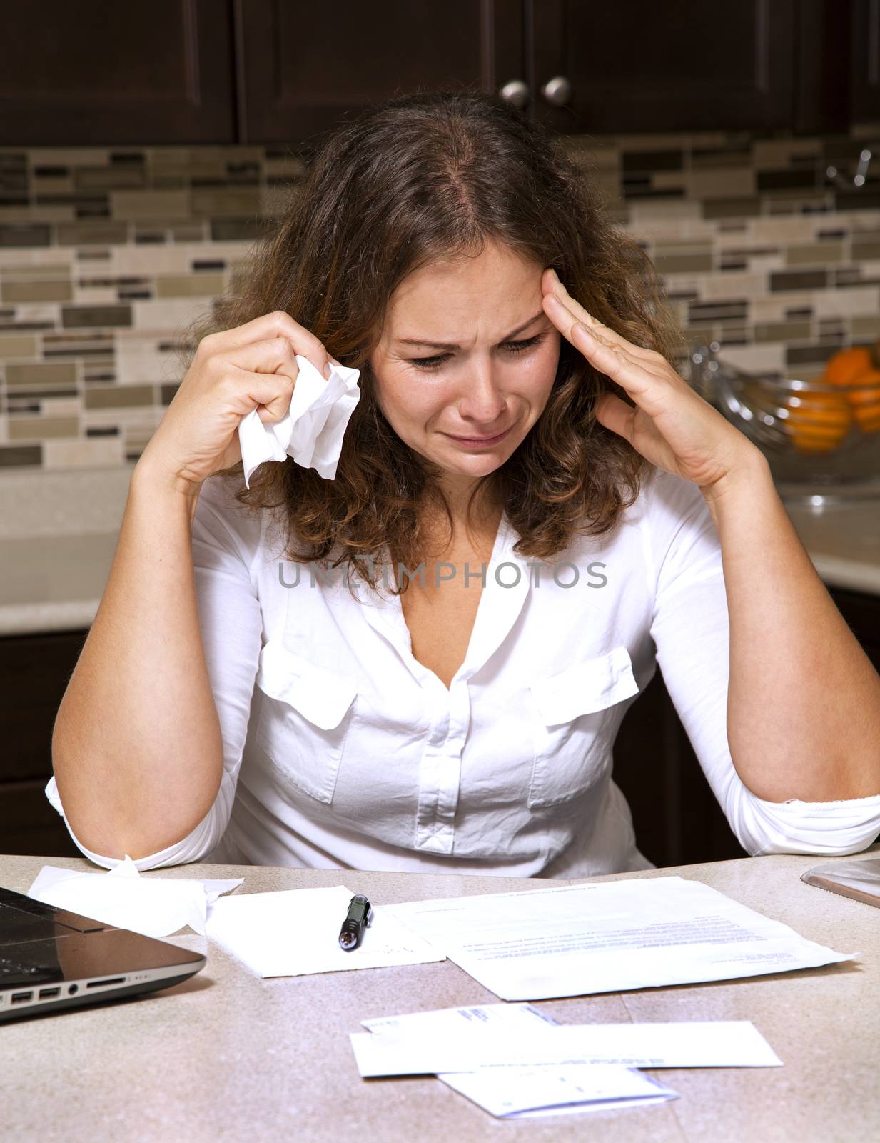 stressed woman looking at bills while sitting in the kitchen 