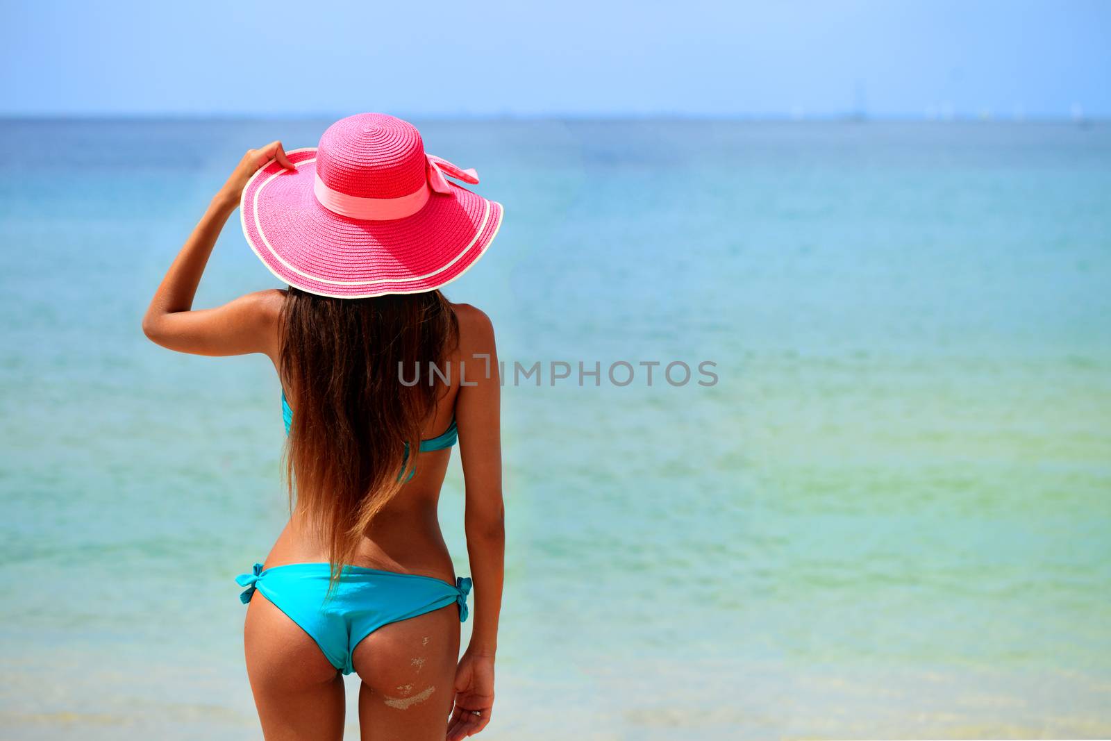 Woman in big hat sitting on beach by the sea