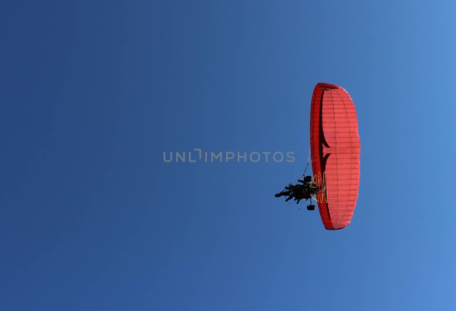 Paraglider and a passenger on a red paraglider with a motor are flying in the blue sky.