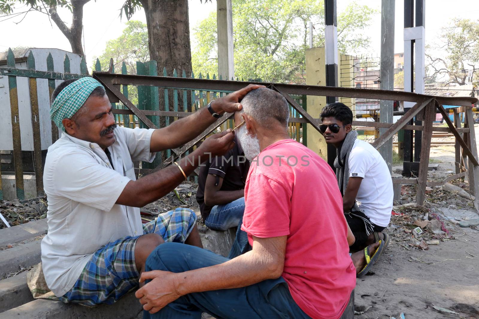 Street barber shaving a man using an open razor blade on a street in Kolkata, West Bengal, India