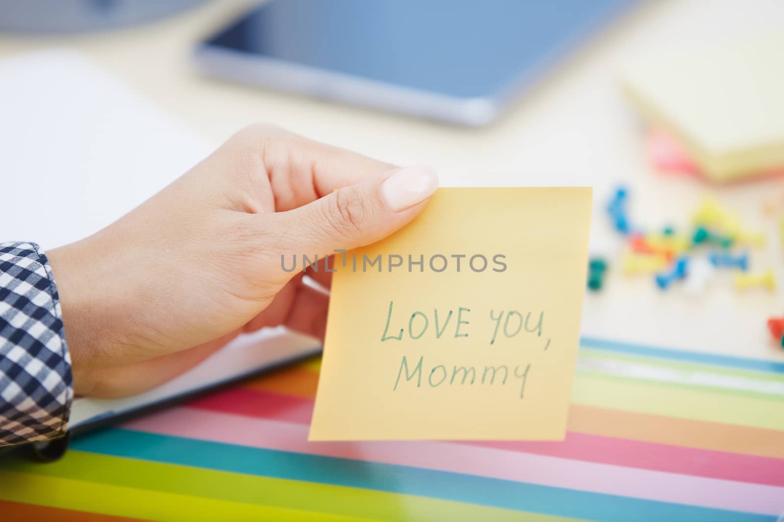 Human hand holding adhesive note with Love you mommy text
