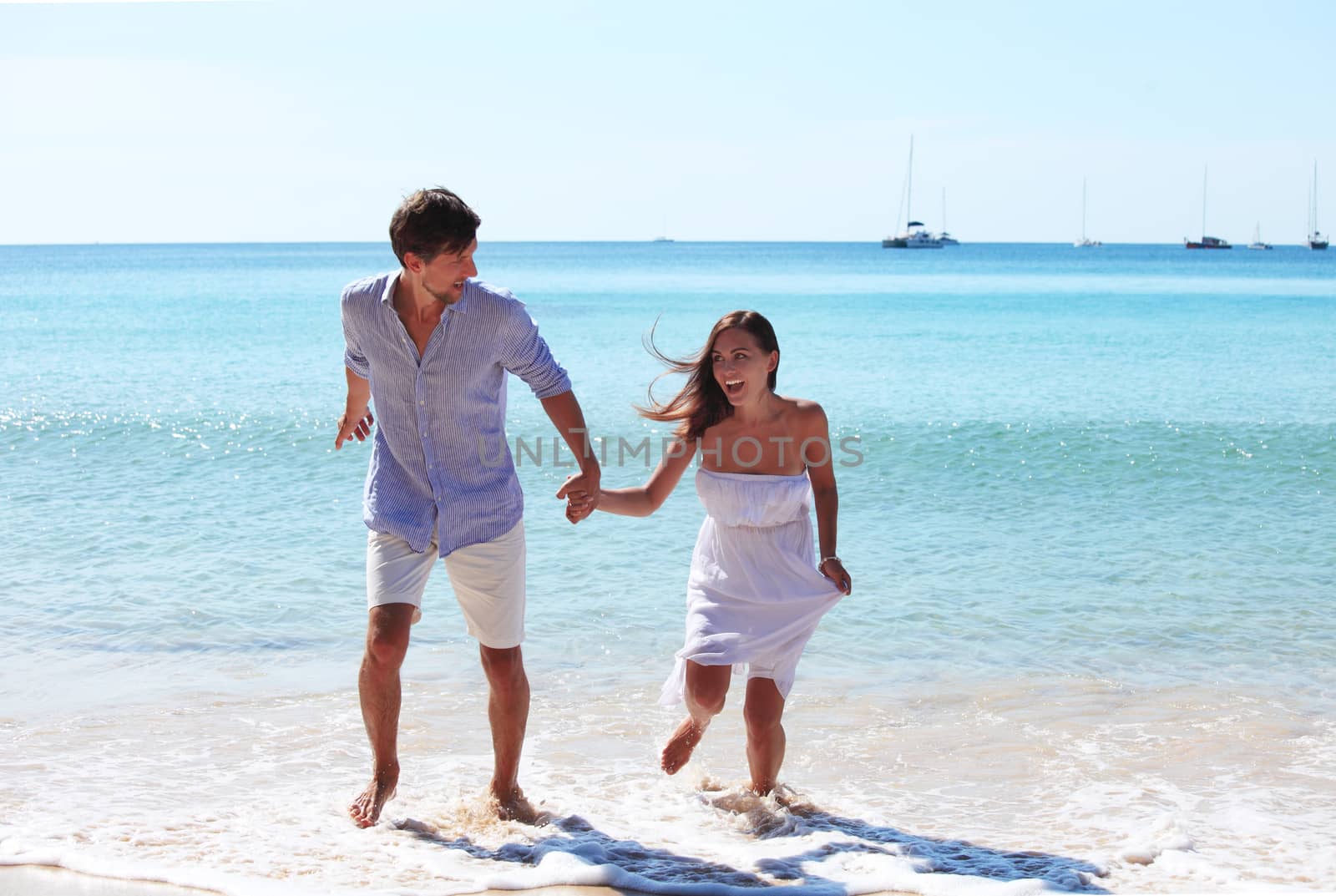 Cheerful couple walking on beach on blue sea background