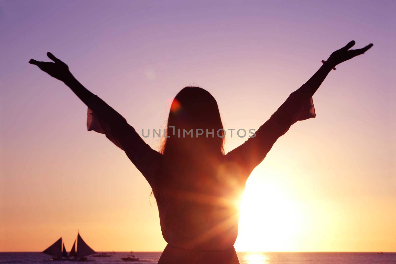 Woman with raised hands at sunset by the sea