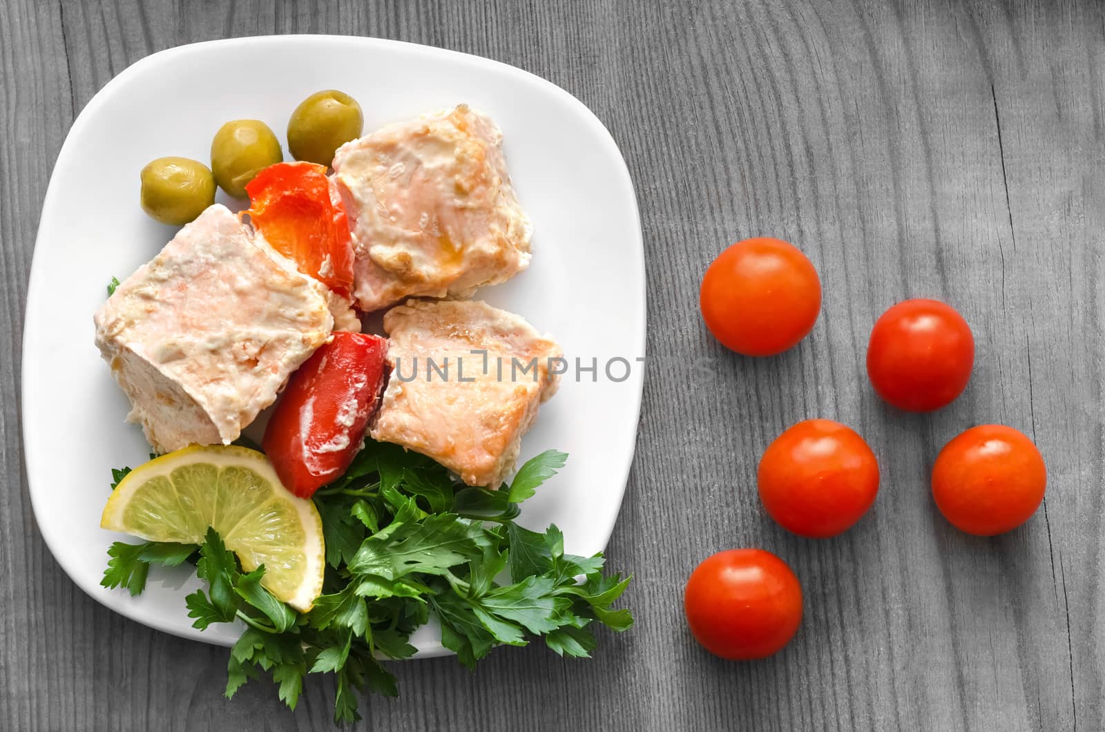 Salmon, grilled with lemon and vegetables. On a white plate and a gray wooden background.