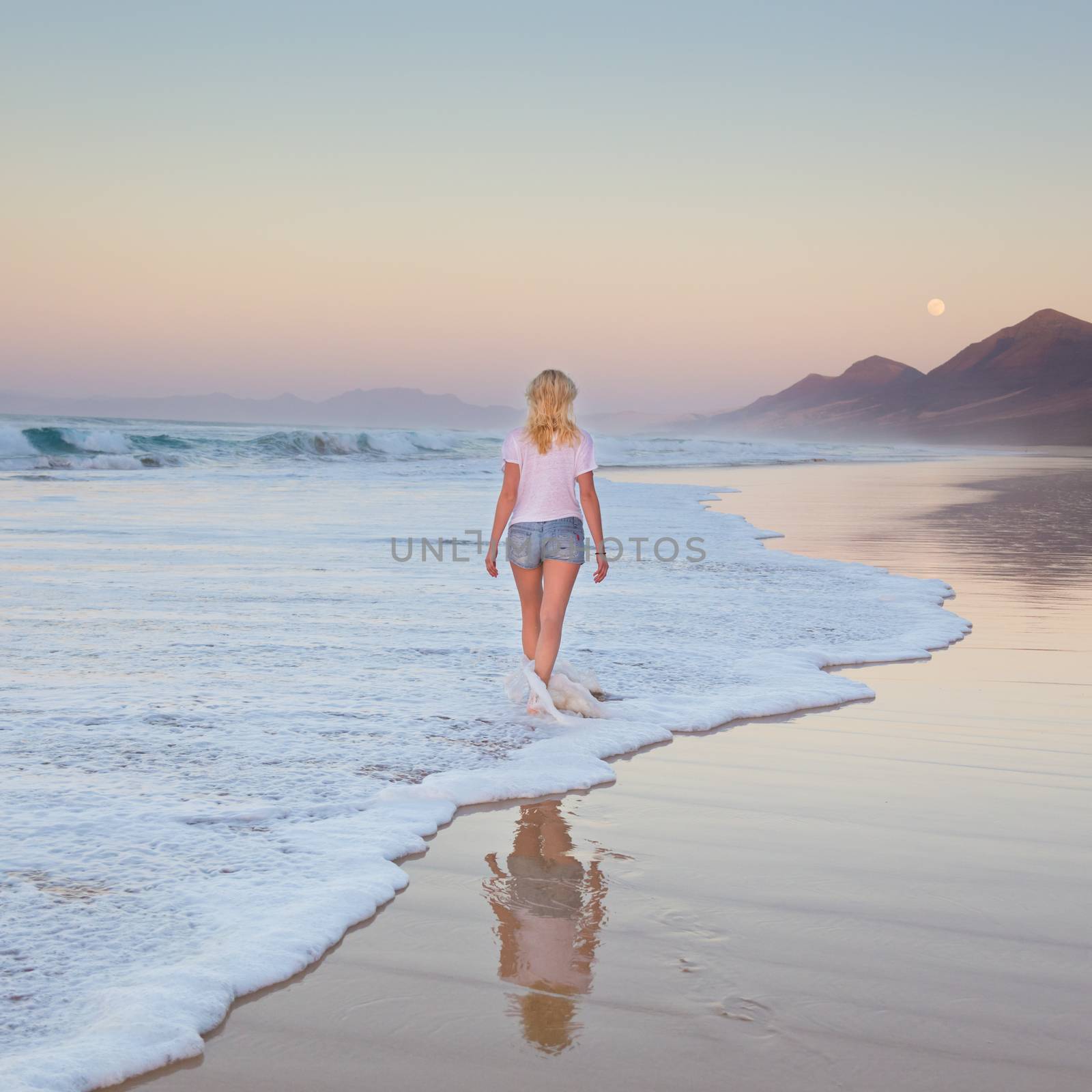 Lady walking on sandy beach in sunset. by kasto