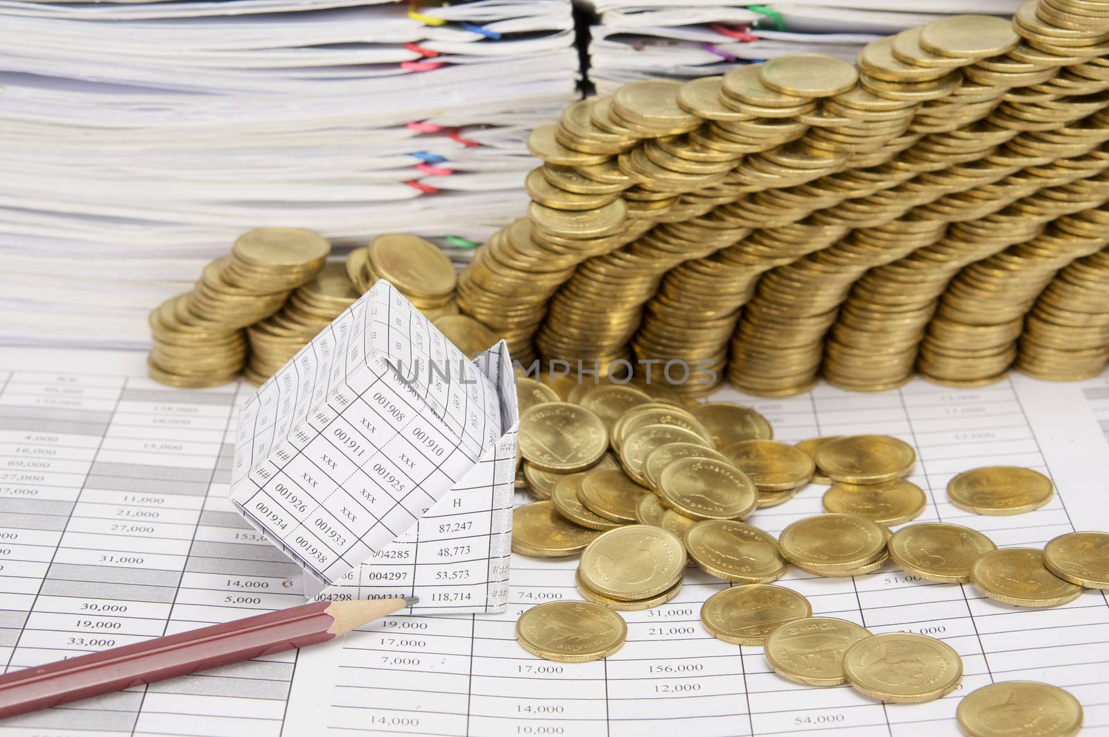 Close up pencil and bankruptcy of house on finance account have step pile of gold coins collapse and pile of paperwork as background.