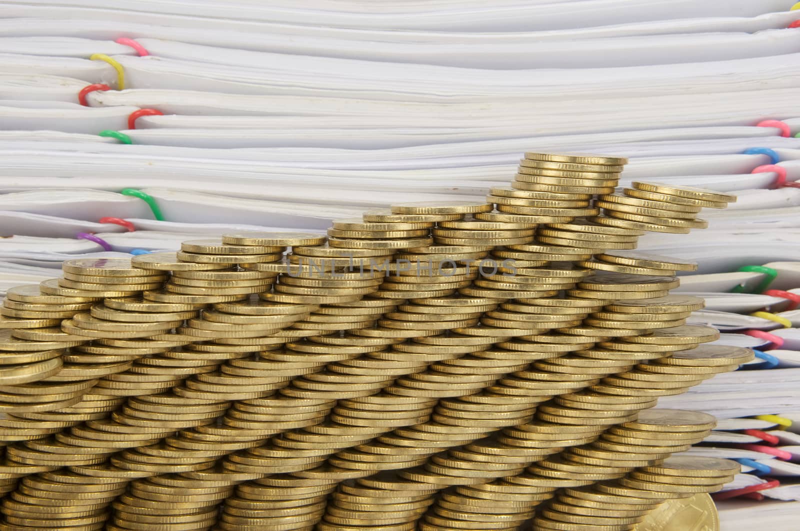 Step pile of gold coins collapse with pile of paperwork as background.