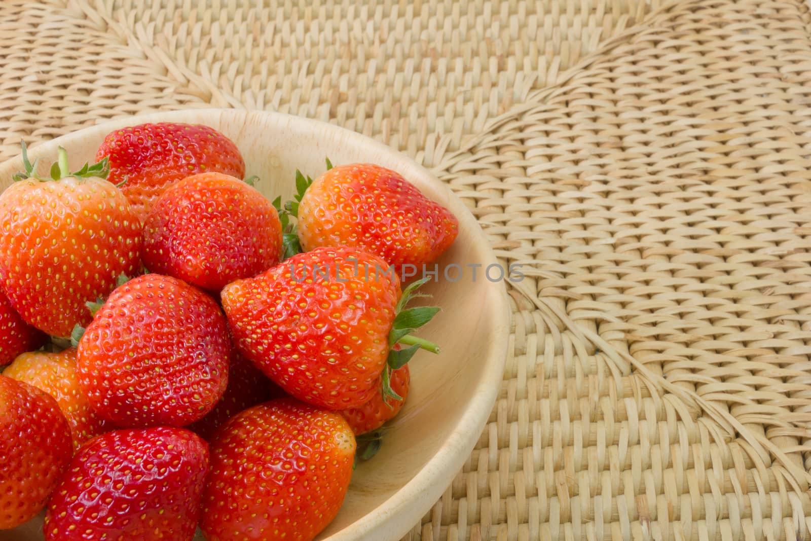 fresh strawberry in wooden bowl on wickerwork background by chingraph