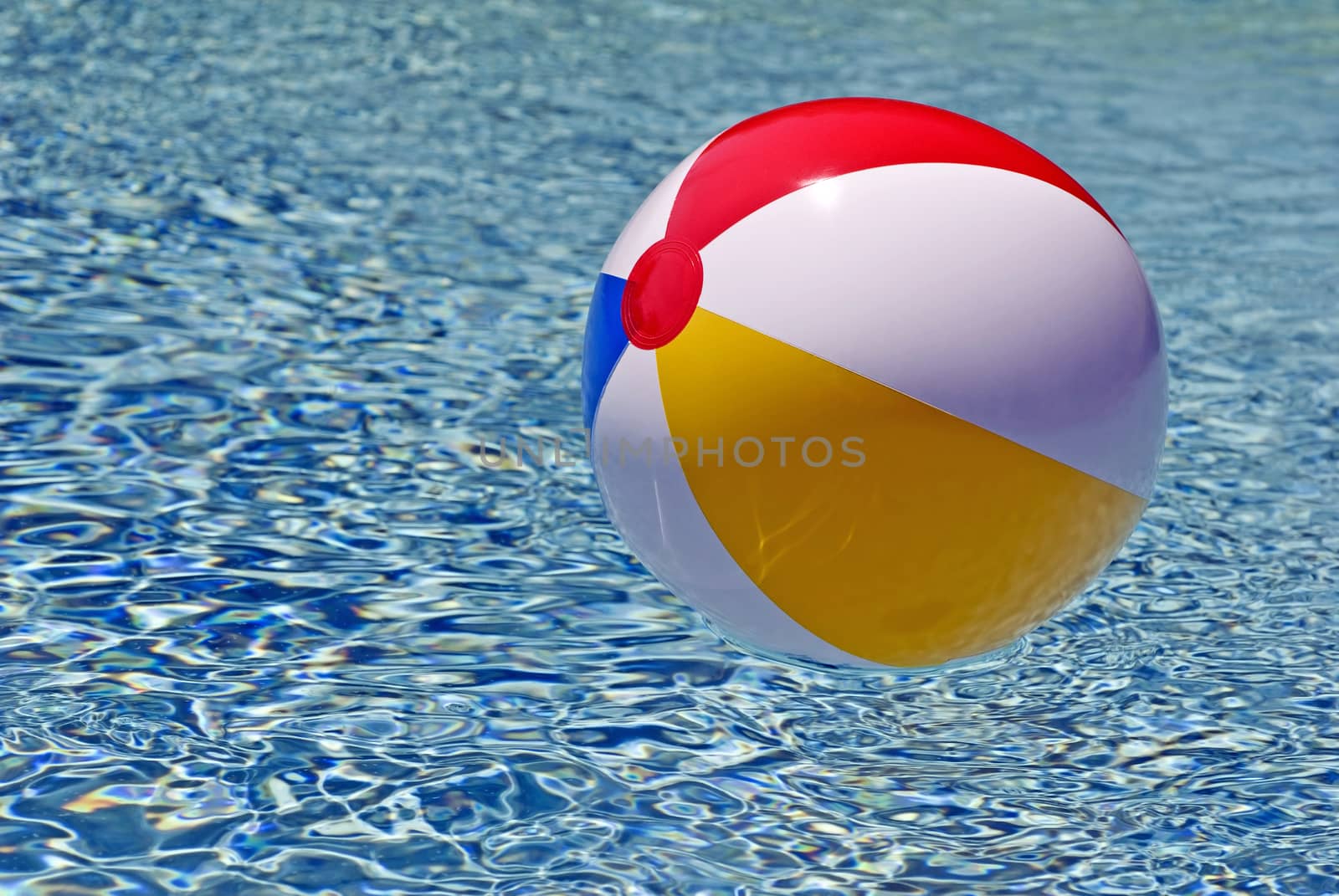 Horizontal shot of a brightly colored beach ball floating in blue waters in swimming pool
