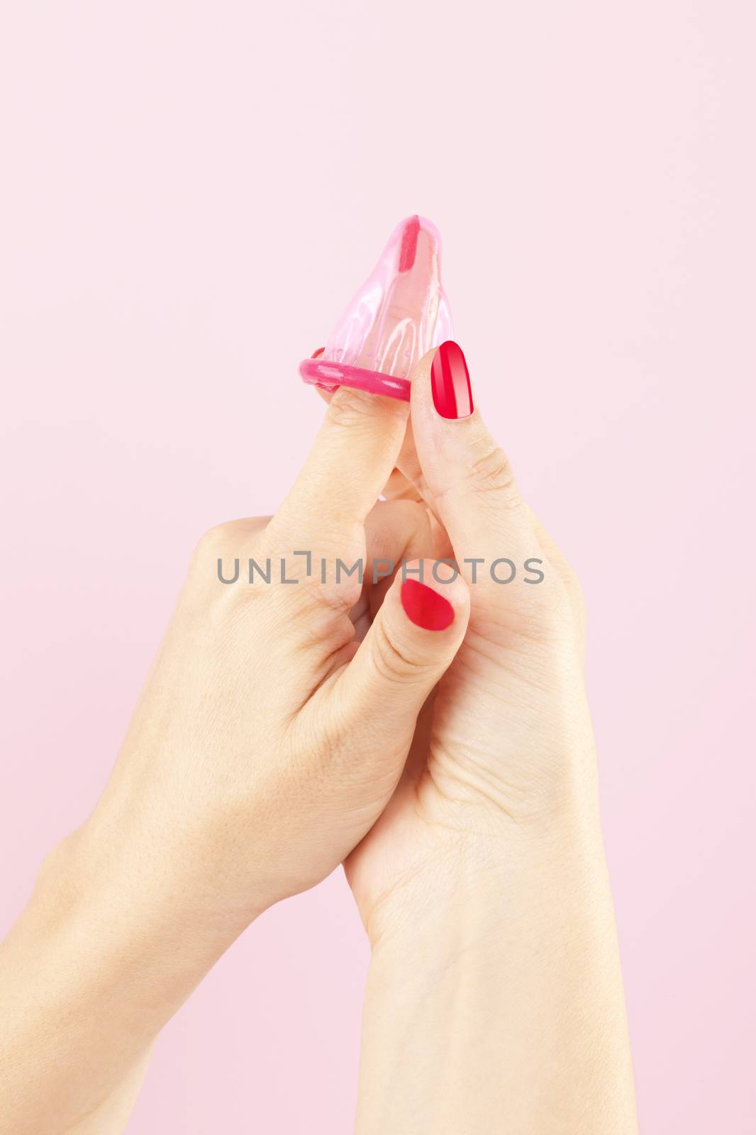 Female hands with red nails holding a pink condom isolated on pink background. Safe sex and birth control concept. 