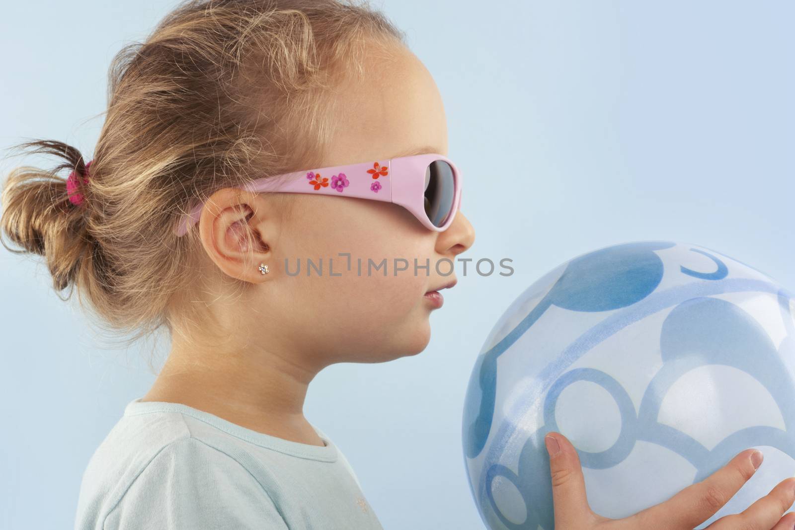 Summer. Adorable beautiful girl with ball and sunglasses against blue background. Summer background.
