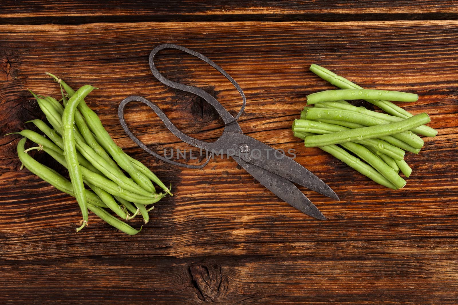 Raw fresh green beans with water drops on brown wooden textured table. Fresh vegetable eating. 
