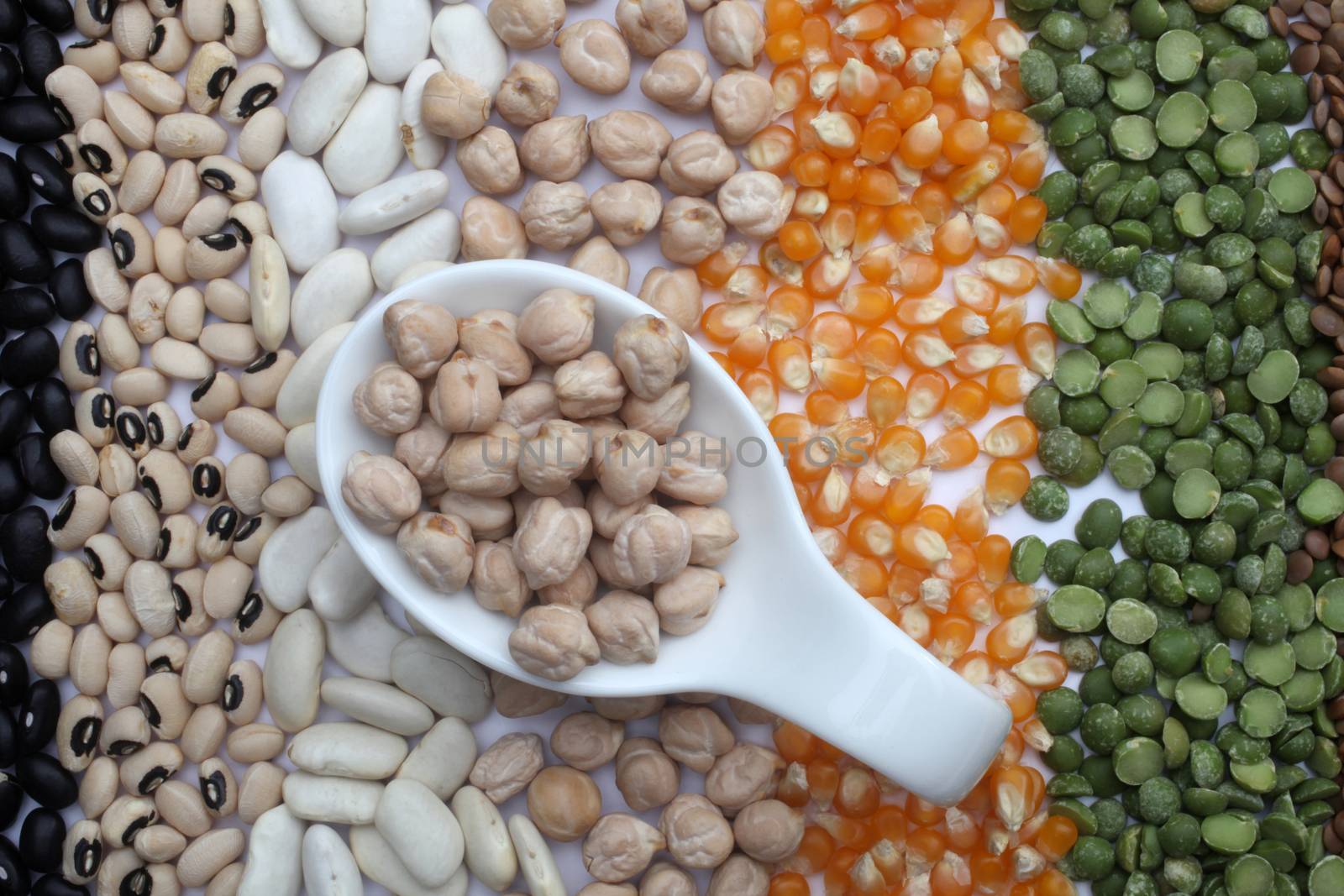 Ceramic spoon with chickpeas over seeds and grains background
