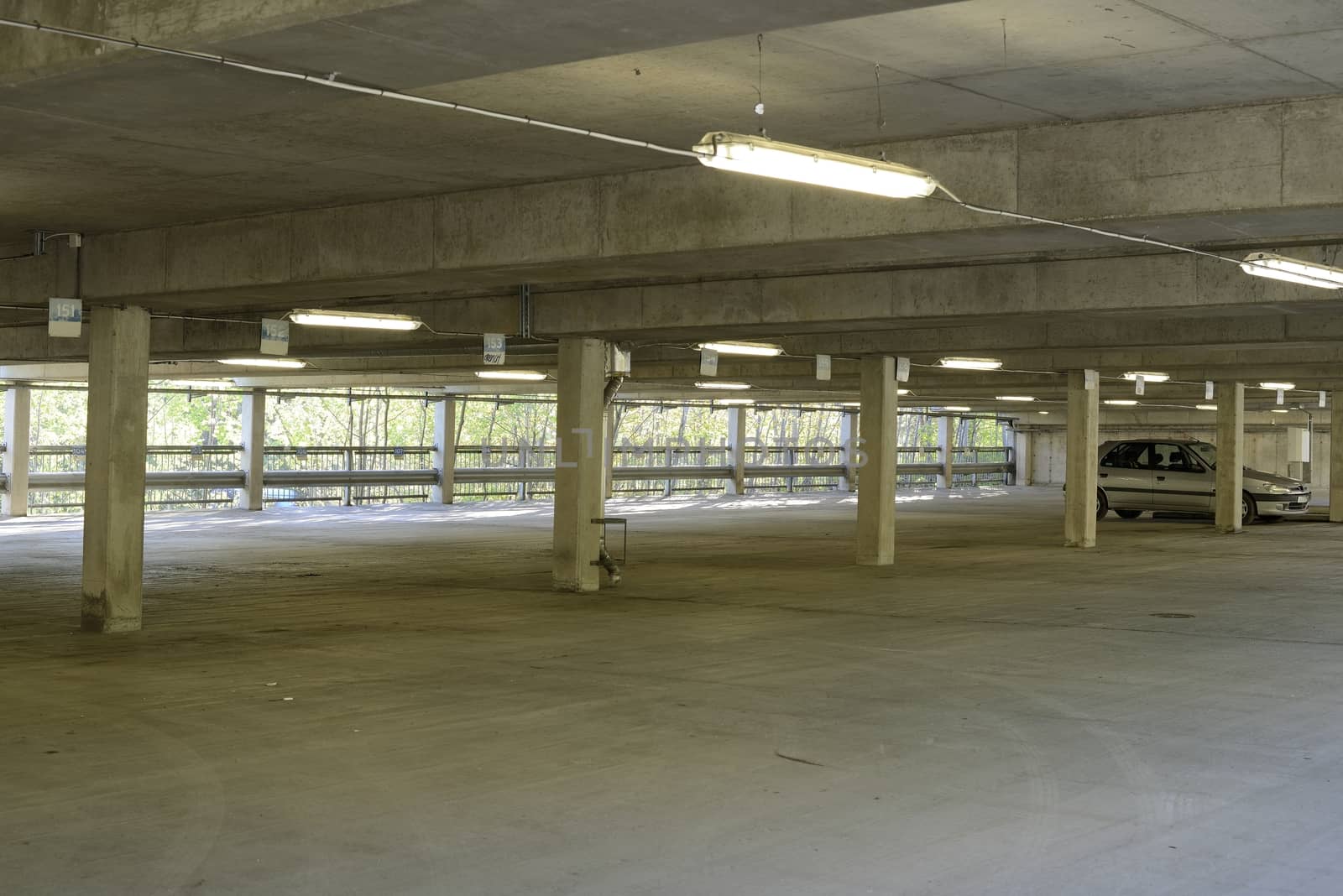 Lit by the sickly glow of cheap fluorescent tubes, an underground parking garage stands almost empty, one car is left.