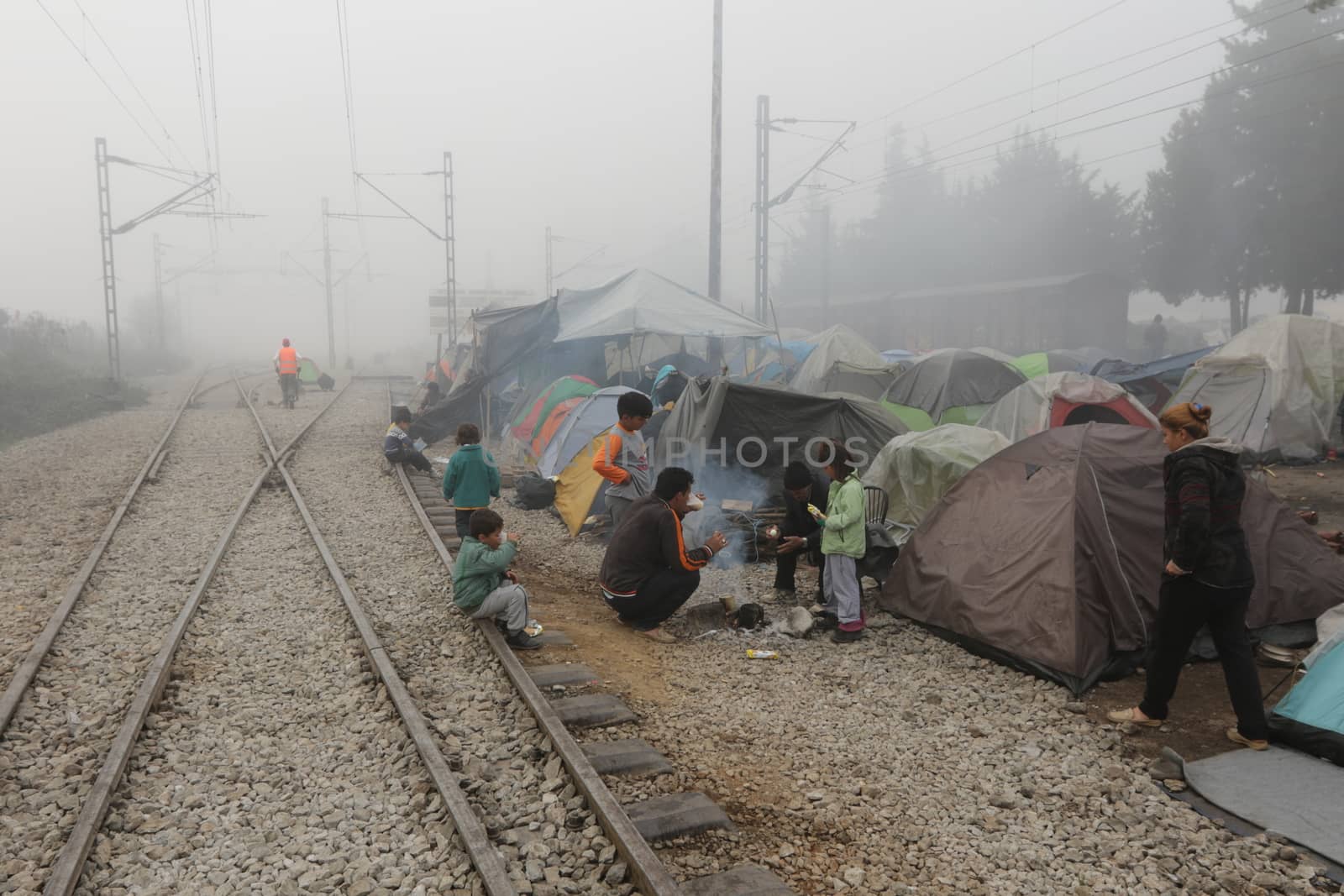 GREECE, Idomeni: Migrants warm up next to a fire near railway tracks in a makeshift camp on April 4, 2016 at Greece-Macedonian border, near Idomeni village where thousands of people are stranded by the Balkan border blockade. Migrants return from Greece to Turkey begun under the terms of an EU deal that has worried aid groups that same day, as Athens struggles to manage the overload of desperate people on its soil. Over 51,000 refugees and migrants seeking to reach northern Europe are stuck in Greece, after Balkan states sealed their borders. Under the agreement, designed to halt the main influx which comes from Turkey, all irregular migrants arriving since March 20 face being sent back, although the deal calls for each case to be examined individually. For every Syrian refugee returned, another Syrian refugee will be resettled from Turkey to the EU, with numbers capped at 72,000.