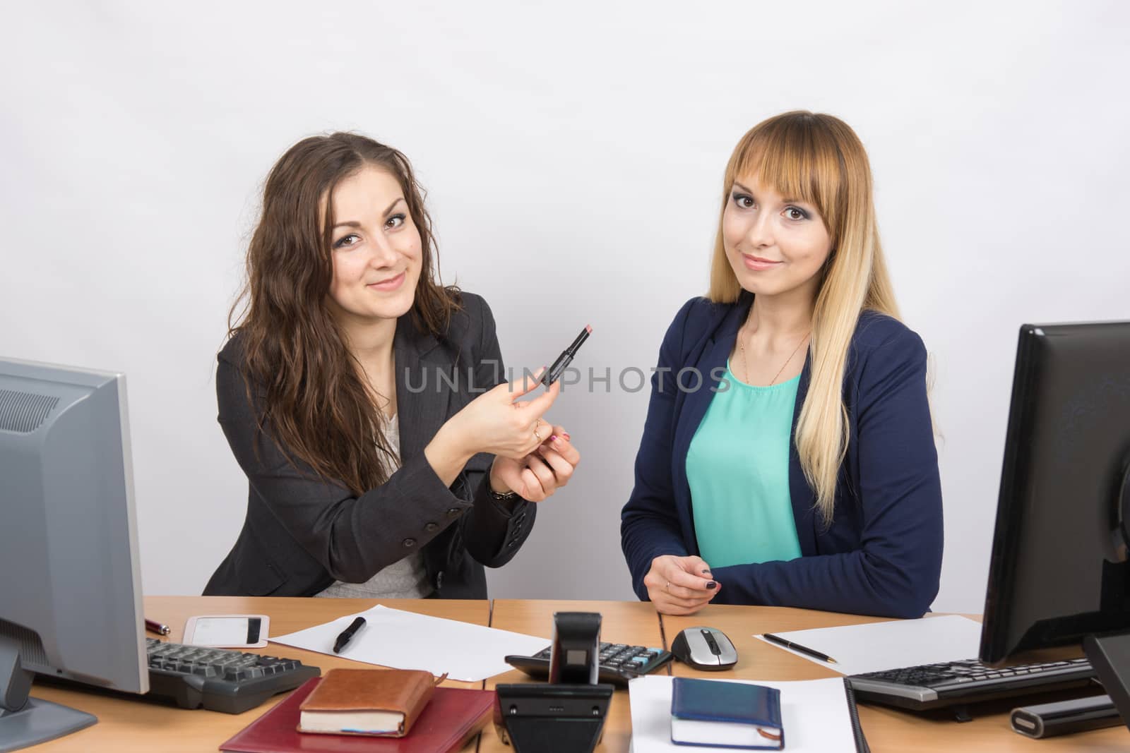 Office girl sitting next to a colleague offers lipstick