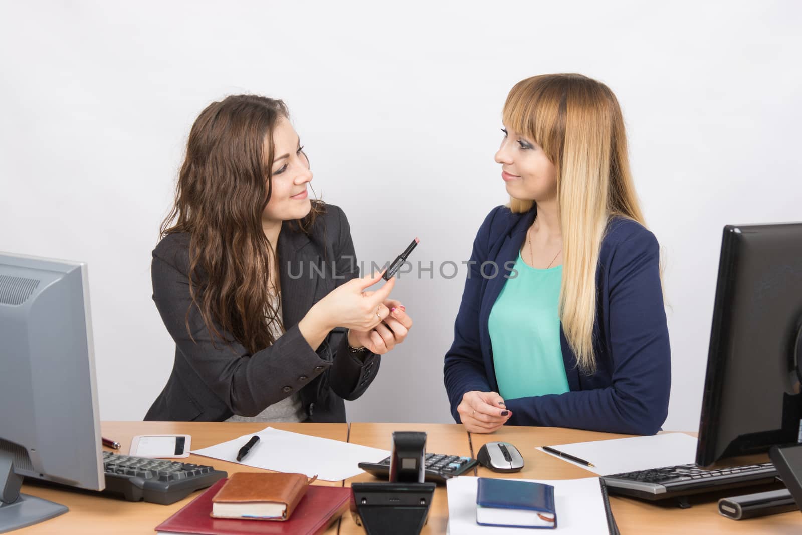 Office employee offers to a colleague sitting next to lipstick