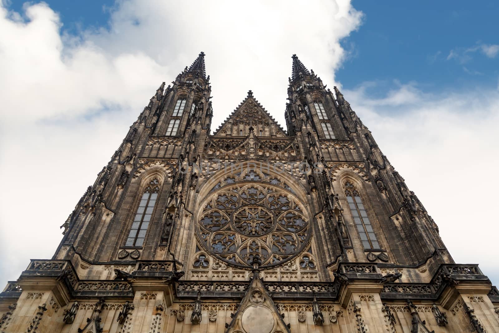 Bottom view of historical gothic St. Vitus Cathedral in old town of Prague, found in 1344, on cloudy blue sky background.