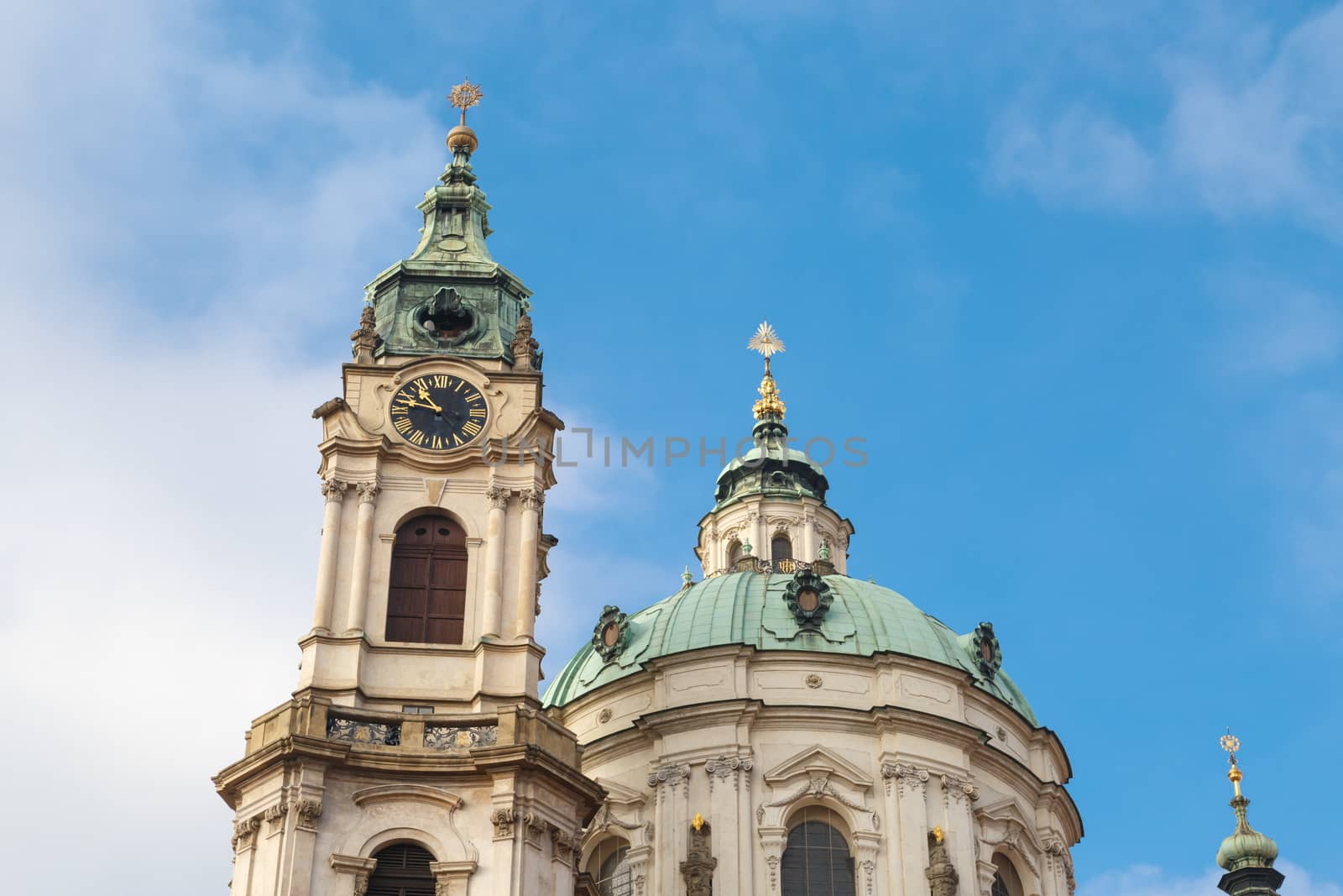 Close up detailed dome view of historical St Nicholas Church in Prague, on cloudy blue sky background.