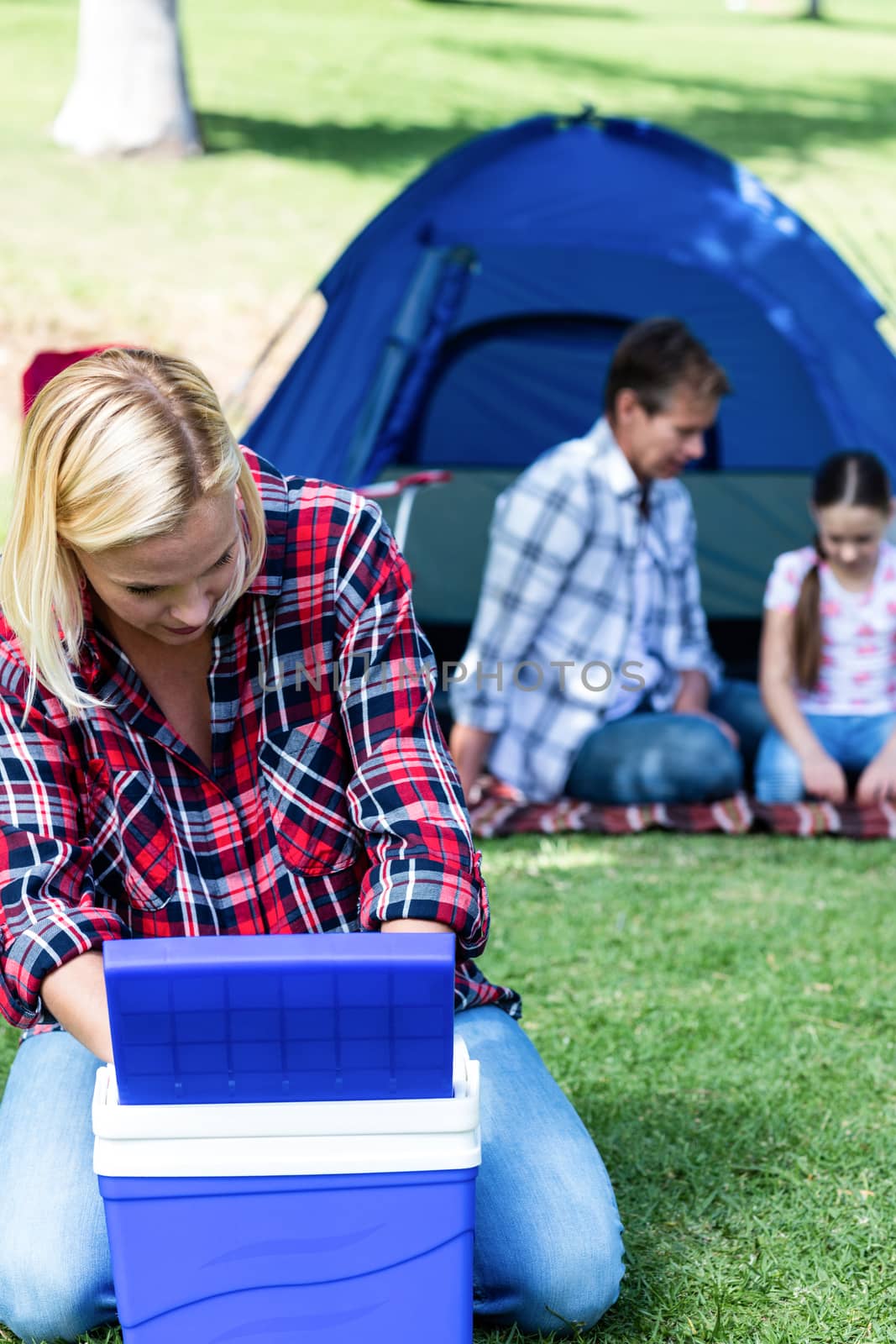 Woman looking into the cool box outside a tent and family sitting in background