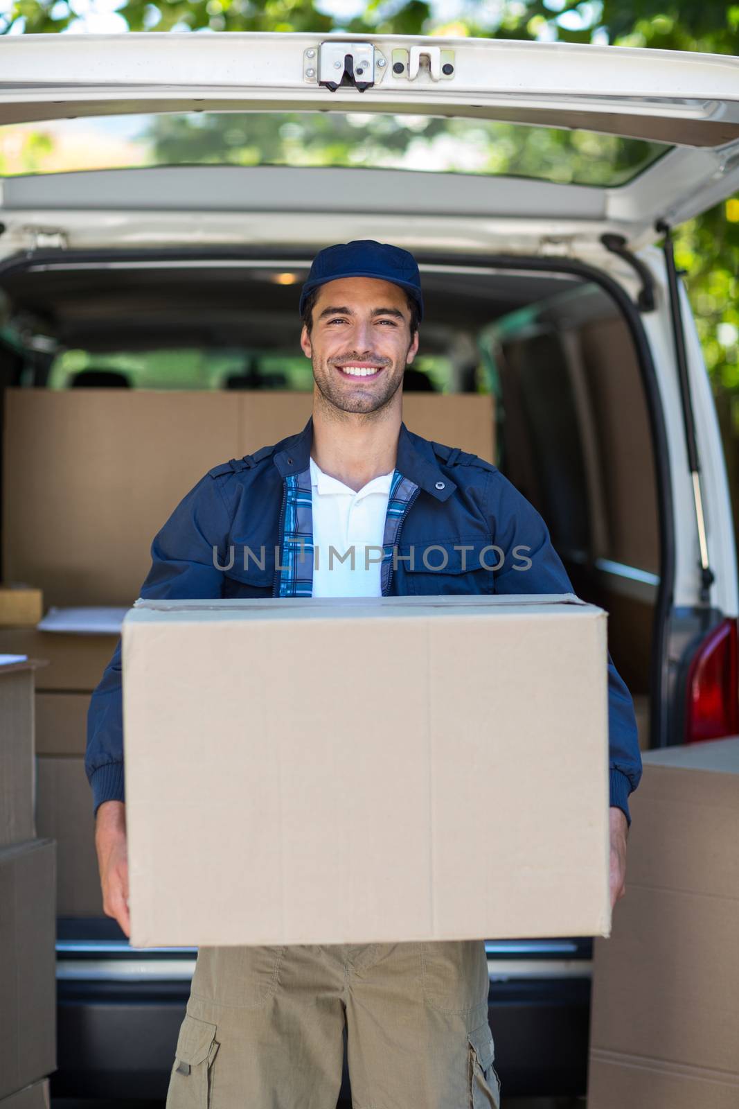 Portrait of smart delivery man carrying cardboard box by Wavebreakmedia