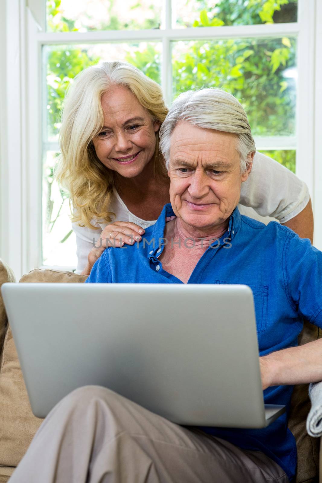 Senior couple using laptop while sitting on sofa against window at home