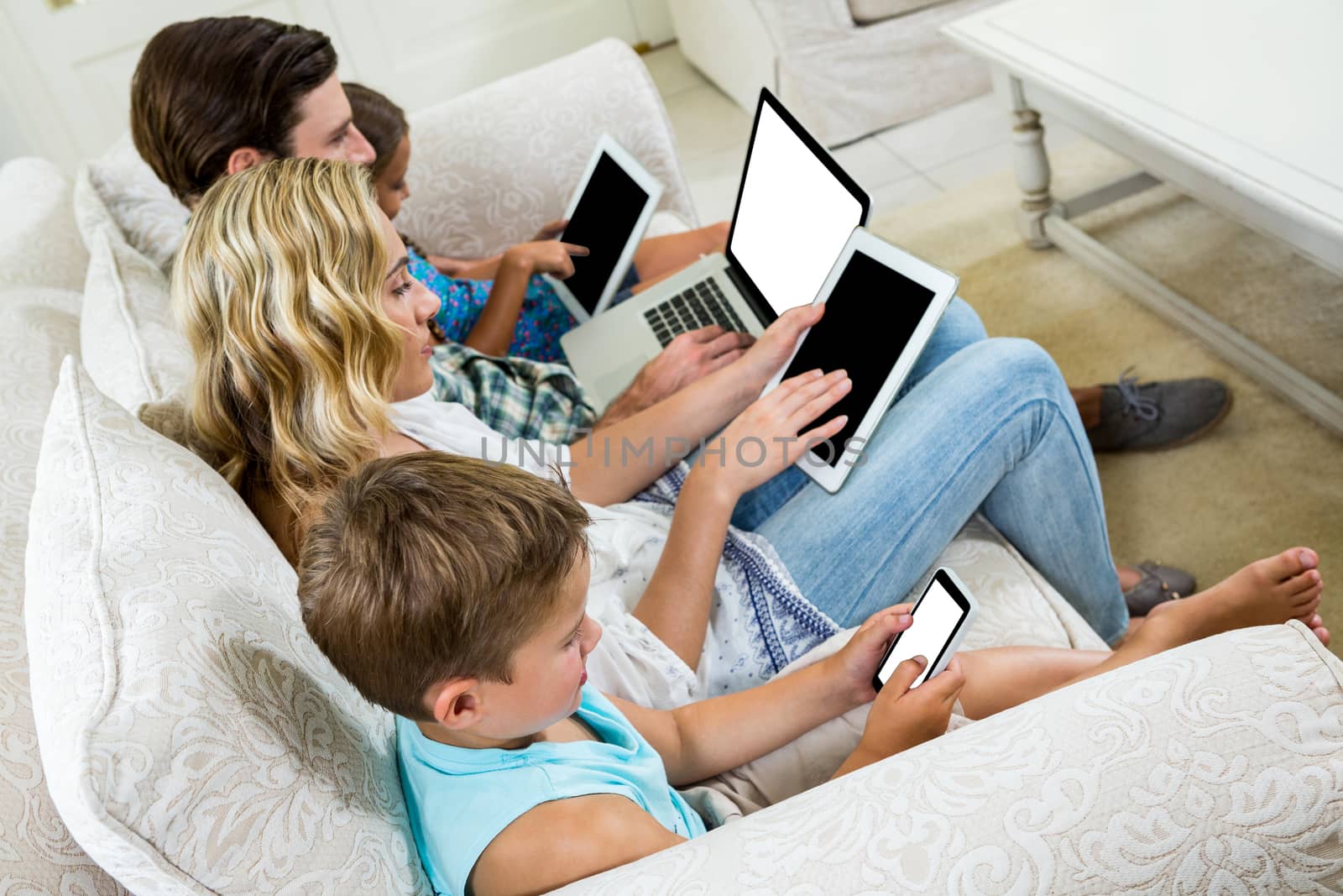 Family using various technologies while sitting on sofa by Wavebreakmedia