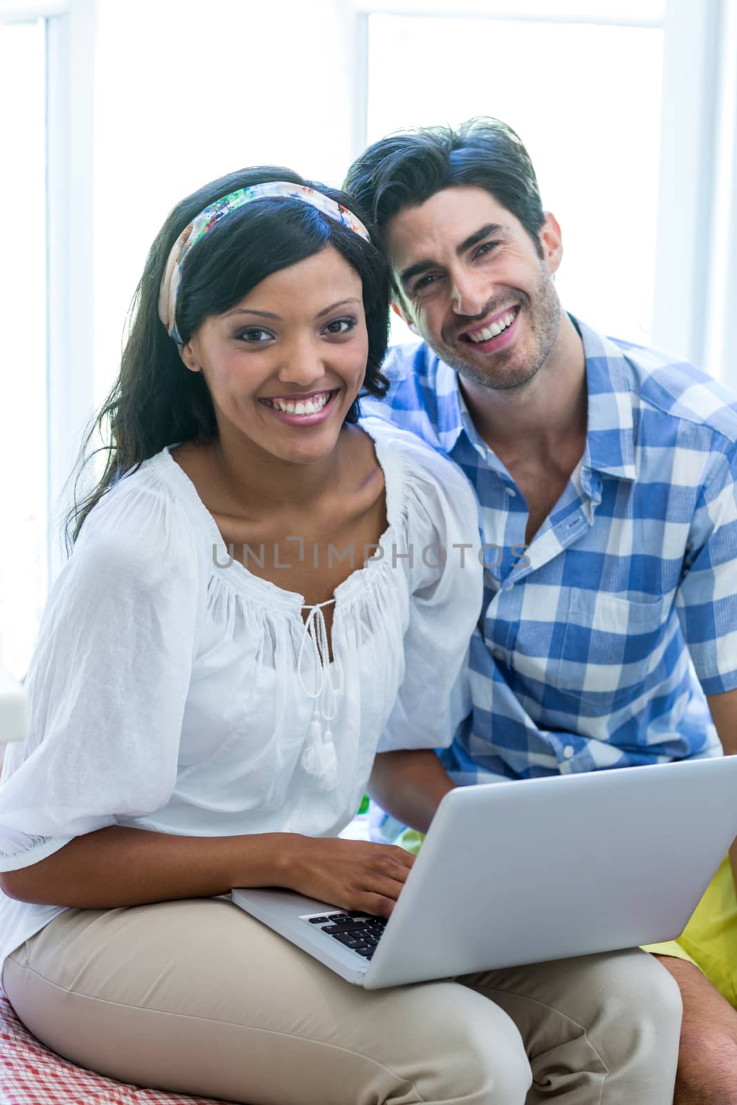Portrait of young couple sitting on bed and using laptop at home