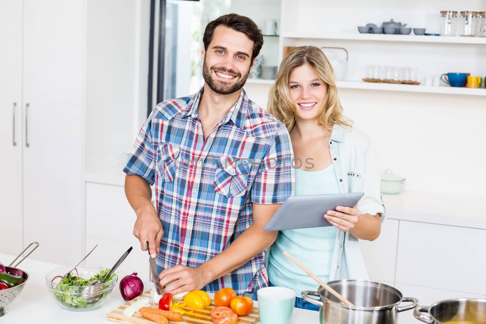 Portrait of young couple chopping vegetable and holding digital tablet in the kitchen