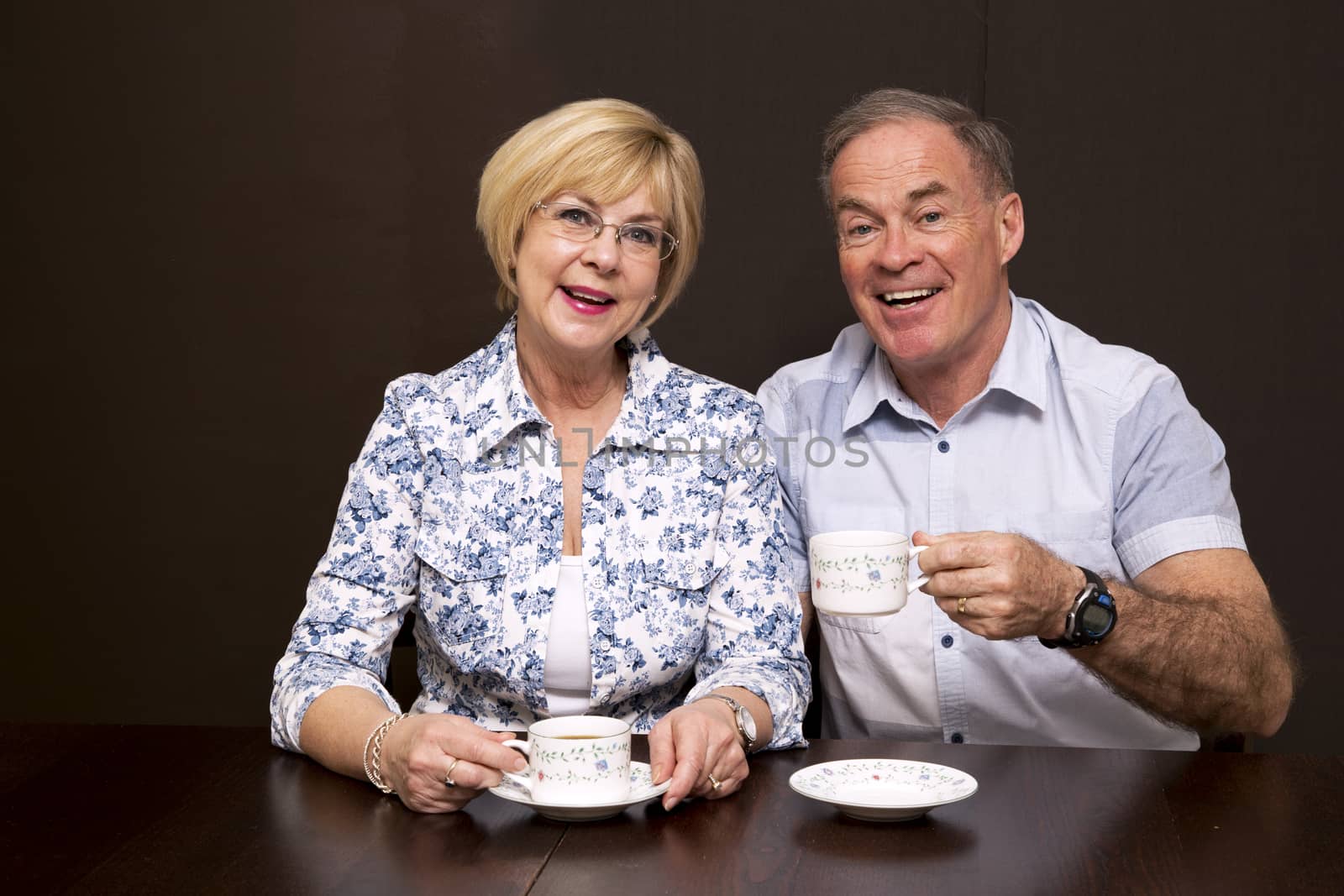 retired couple sitting by the table having coffee dark background