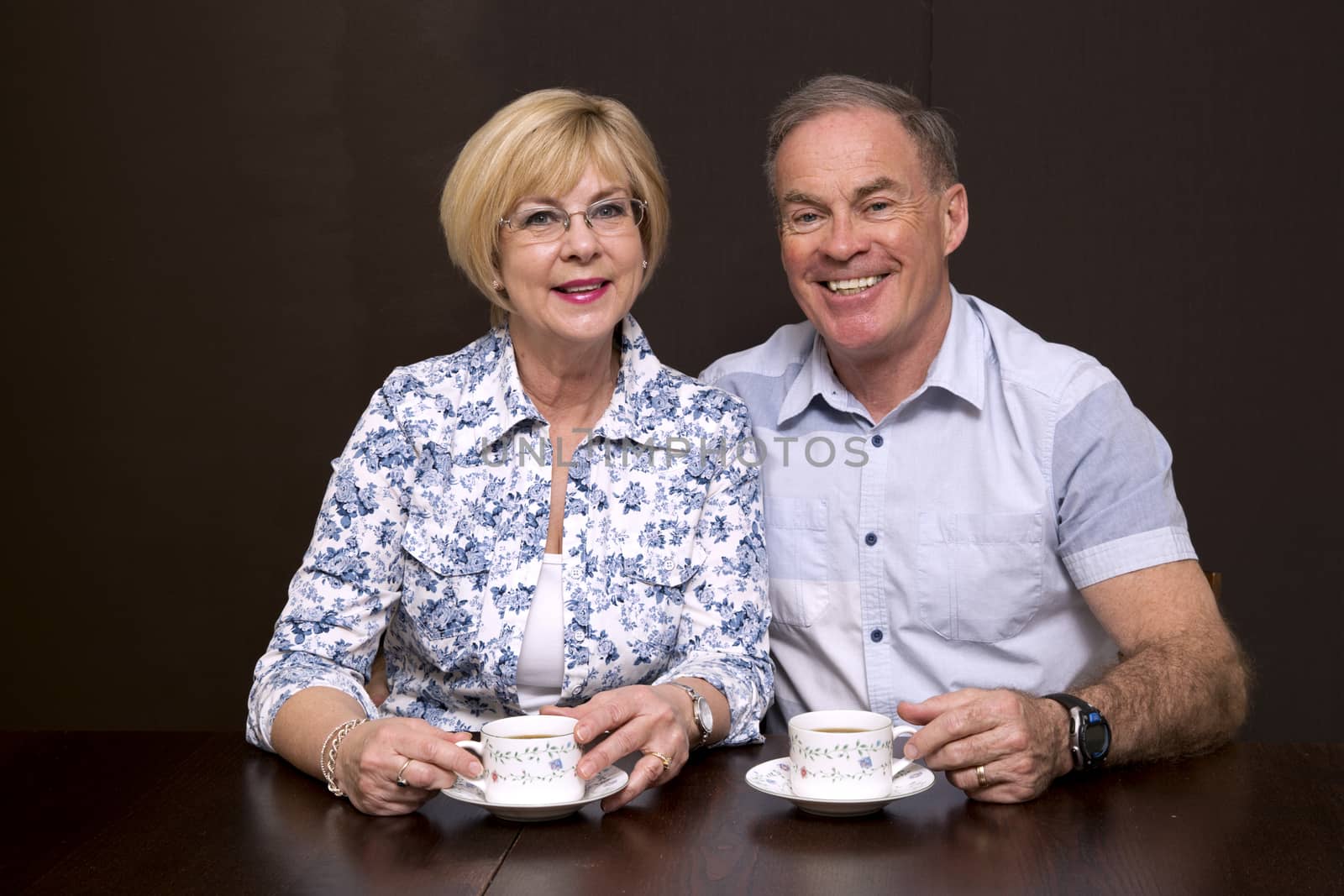 retired couple sitting by the table having coffee dark background