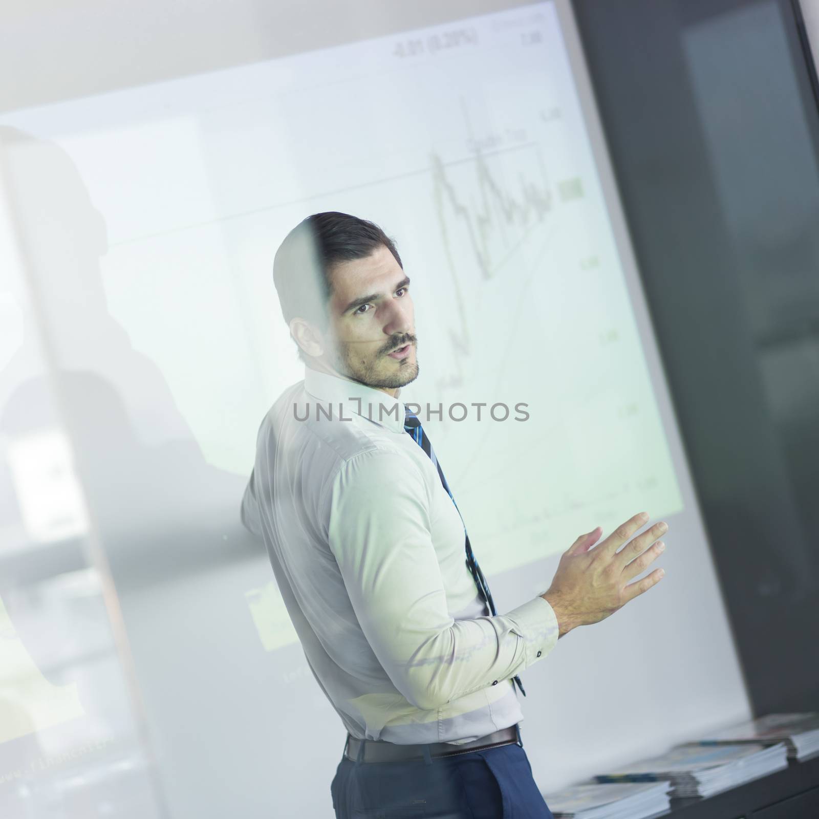 Business man making a presentation in front of whiteboard. Business executive delivering a presentation to his colleagues during meeting or in-house business training. View through glass.