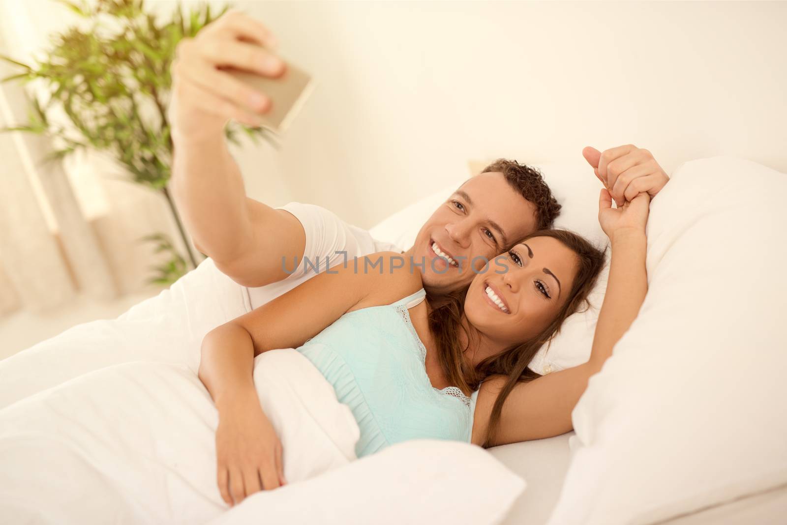 Beautiful young loving couple take a selfie in bed in the morning. 