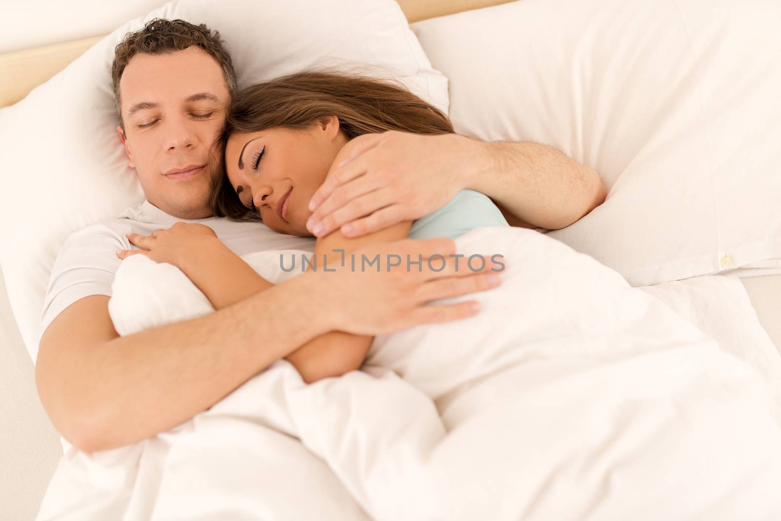 Beautiful young loving couple hugging sleeping in bed. 