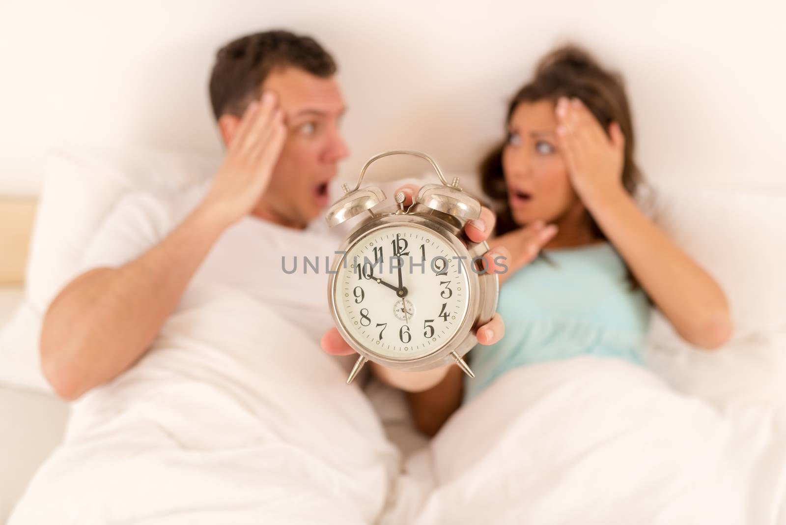 Young couple in bed awaken to the ringing of the alarm clock. They is late in the morning. Focus on the alarm clock, on the foreground.