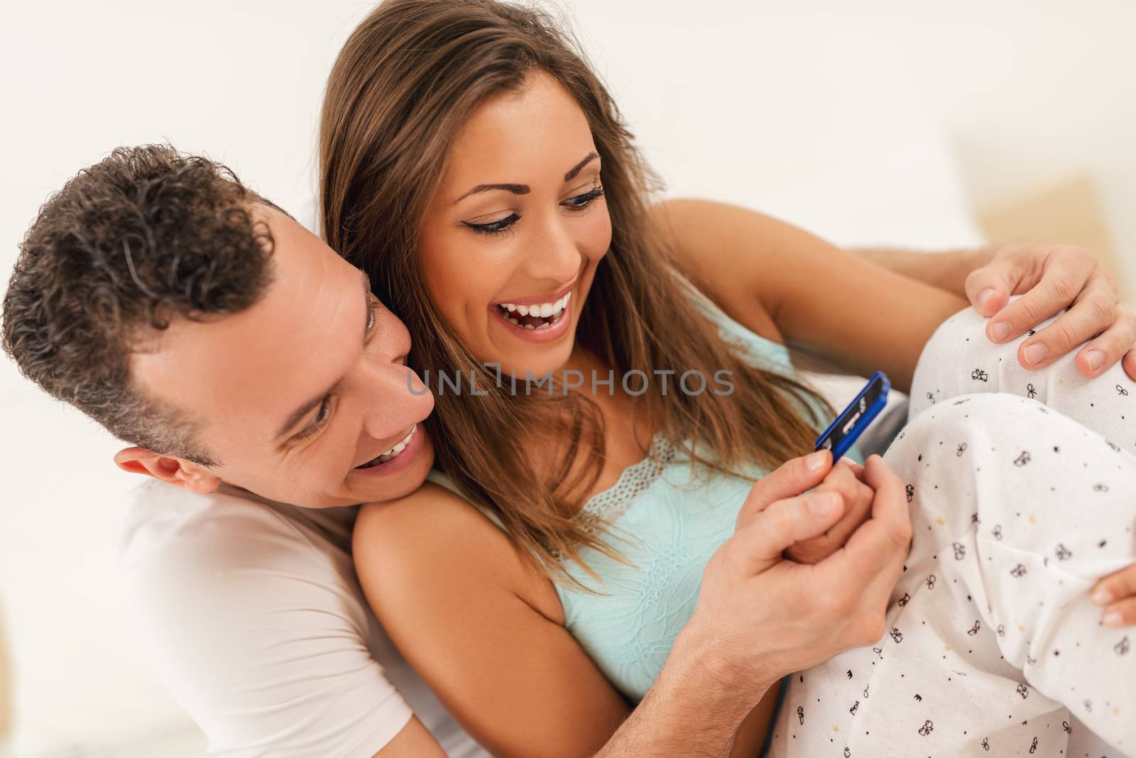 Beautiful young loving couple sitting on the bed with a smile on their face looking at pregnancy test.