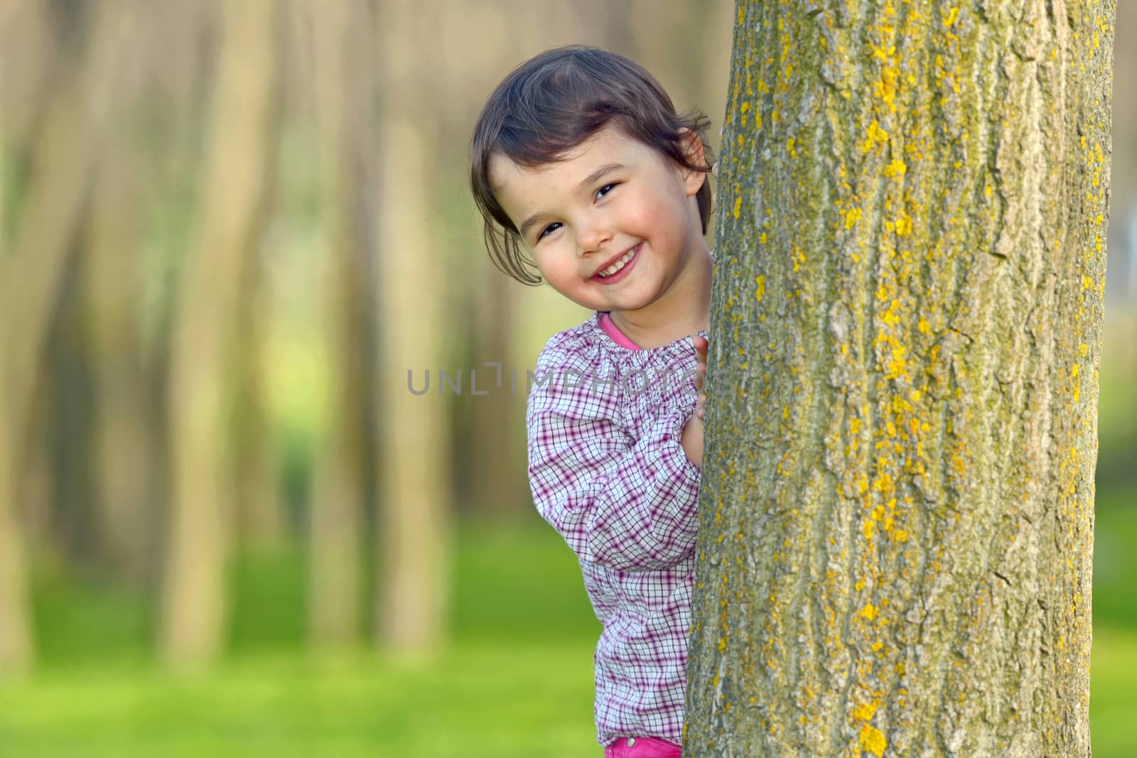 Little girl hiding behind a tree in a forest