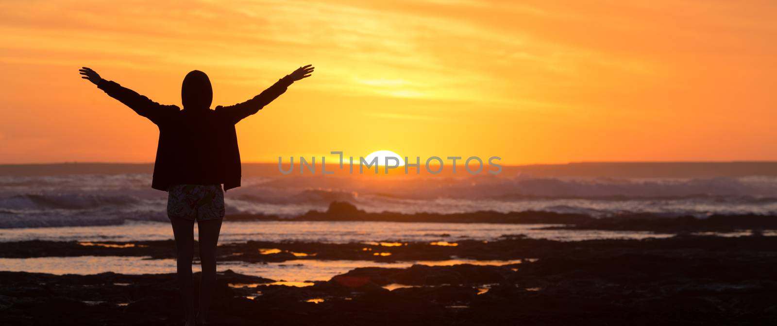 Silhouette of free woman enjoying freedom feeling happy at beach at sunset. Serene relaxing woman in pure happiness and elated enjoyment with arms raised outstretched up. 