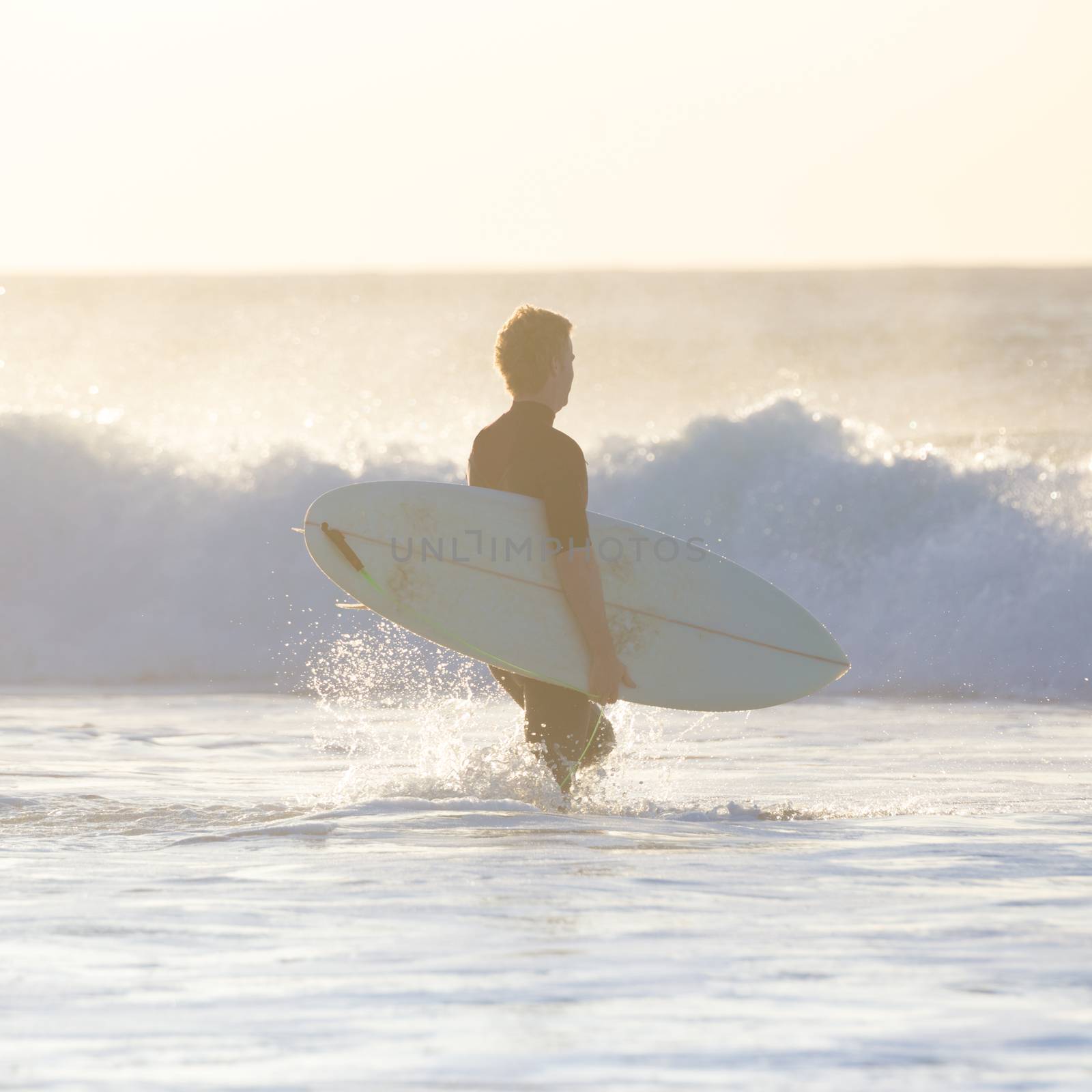 Male surfers on sandy beach with the surfboard in sunset.  