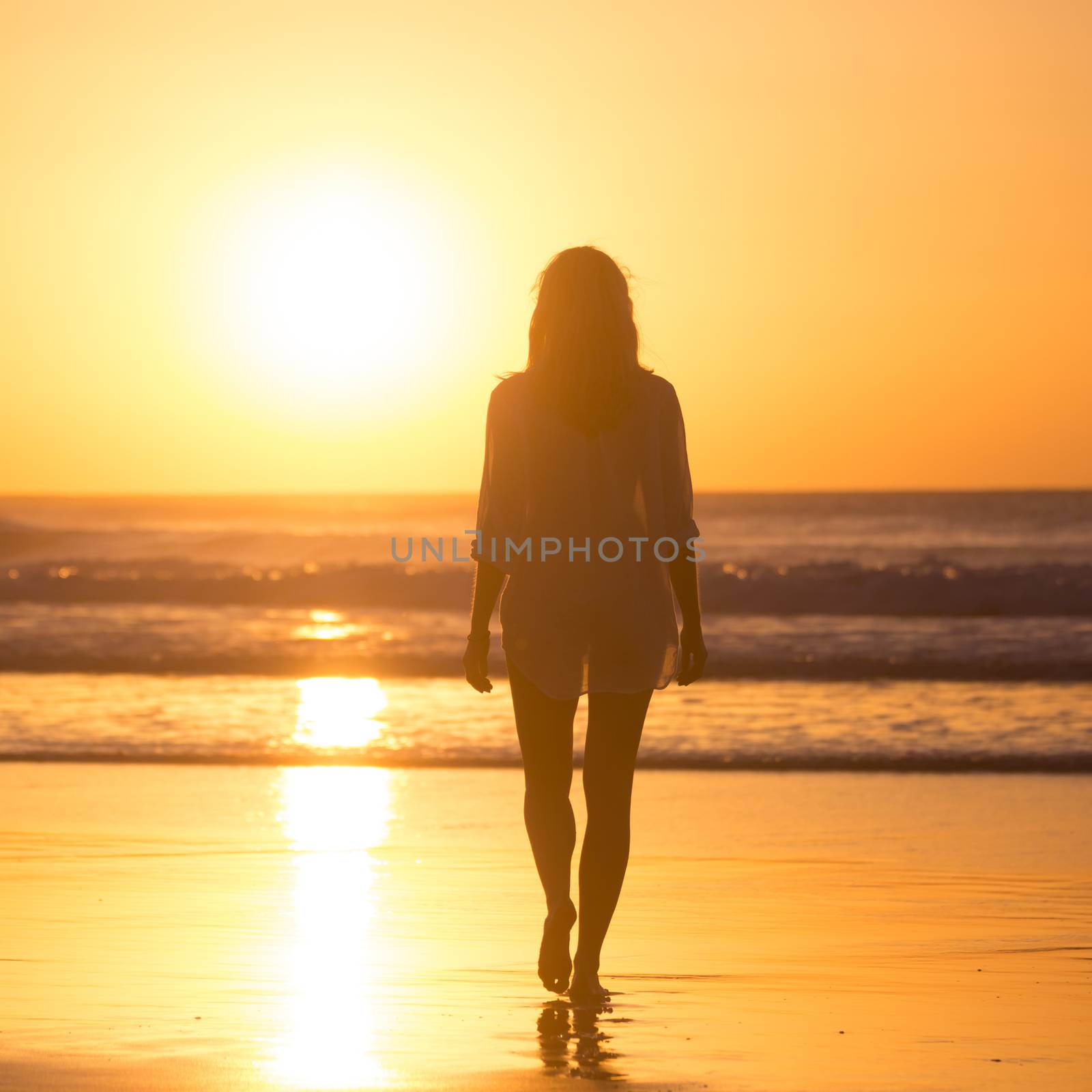 Woman walking on sandy beach in sunset leaving footprints in the sand. Beach, travel, concept. Copy space. Vertical composition.