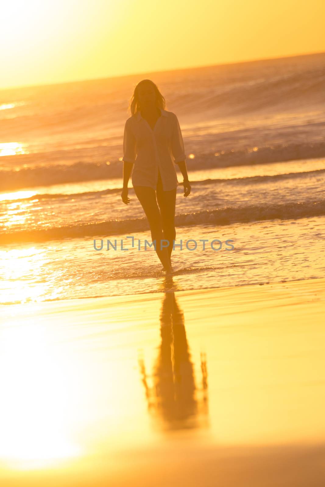 Woman walking on sandy beach in sunset leaving footprints in the sand. Beach, travel, concept. Copy space. Vertical composition.