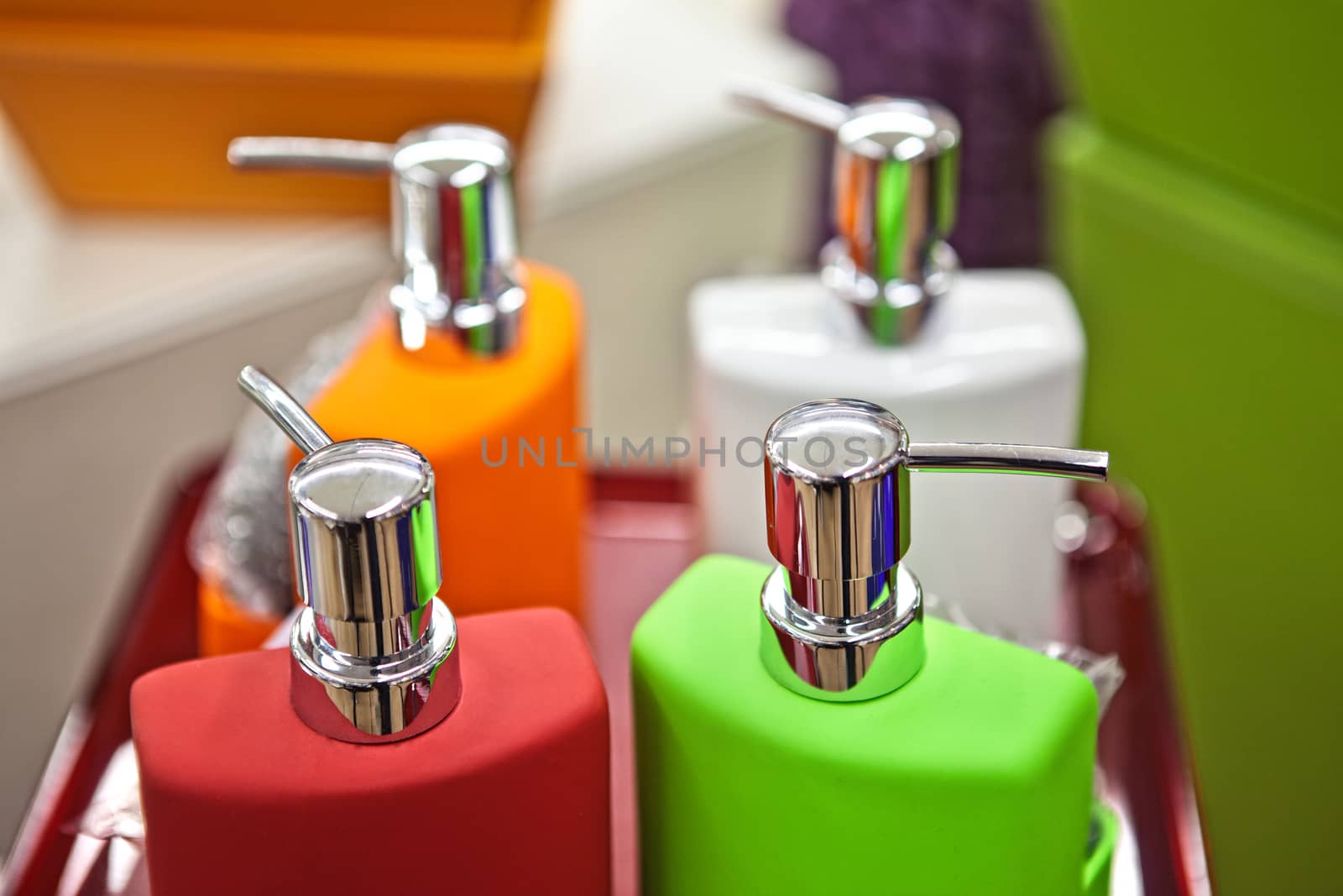 Closeup of many colorful plastic bottled flasks orange pink and green colors standing in raw close to each other with spray top, horizontal picture