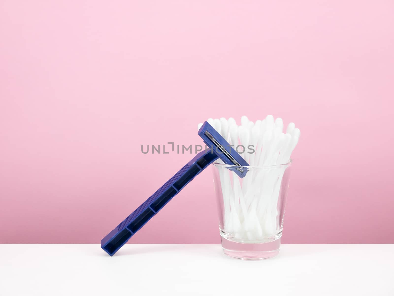 The group of purified white cotton buds in shot glass and dark blue plastic razor.