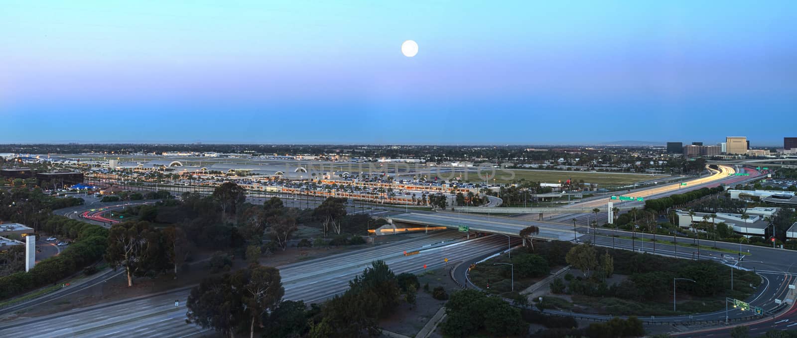 Aerial view of John Wayne Airport in Orange County, California, at sunrise with light trails across the 405 highway in front.