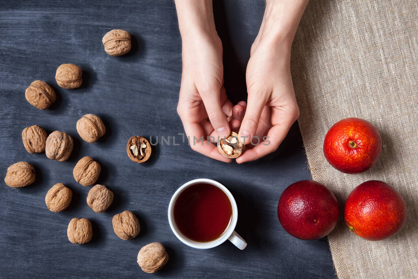 girl holds a walnut in the hands on wooden table with red oranges