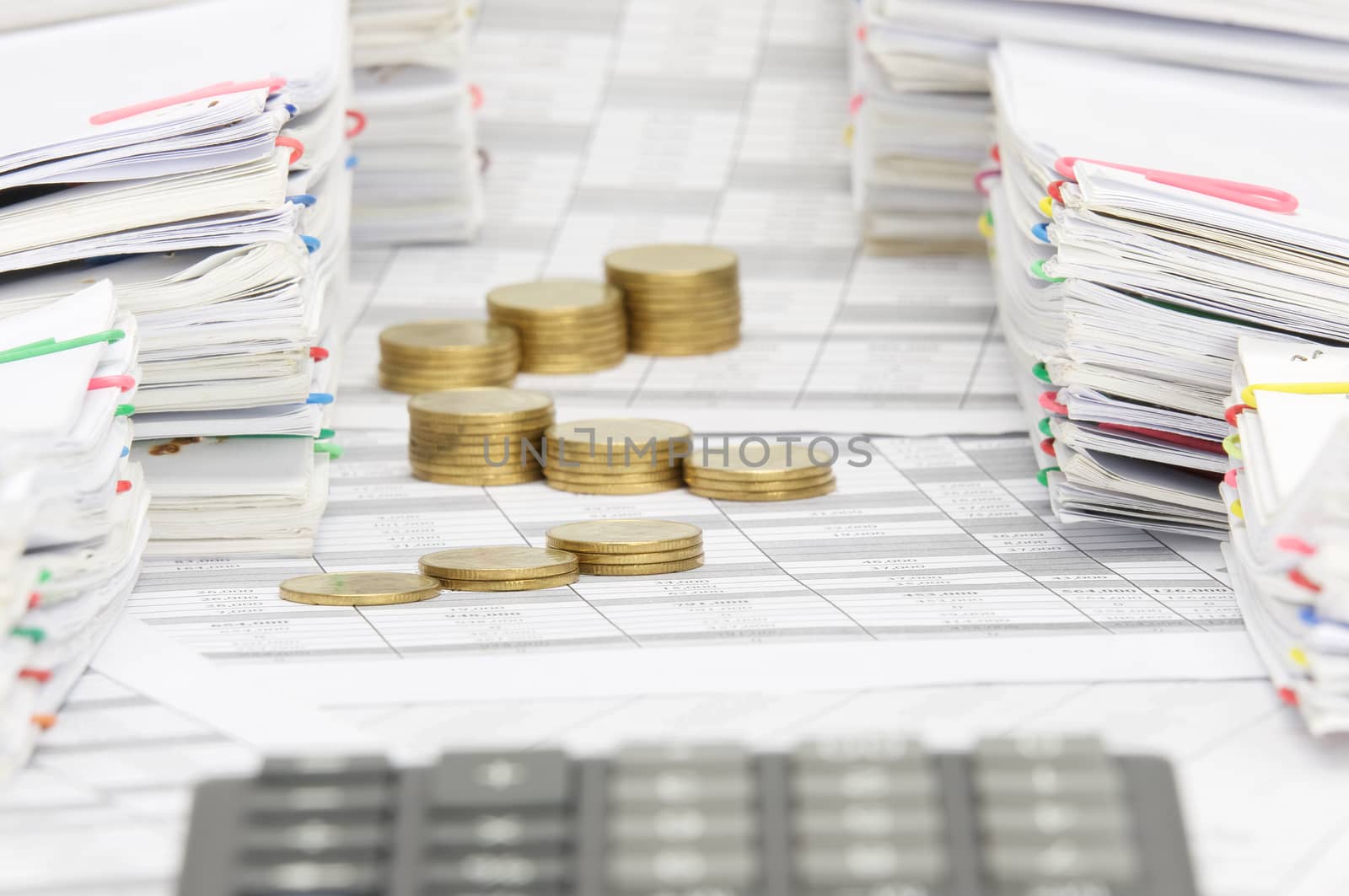 Step pile of gold coins on finance account have blur calculator between pile of paperwork as foreground and background.