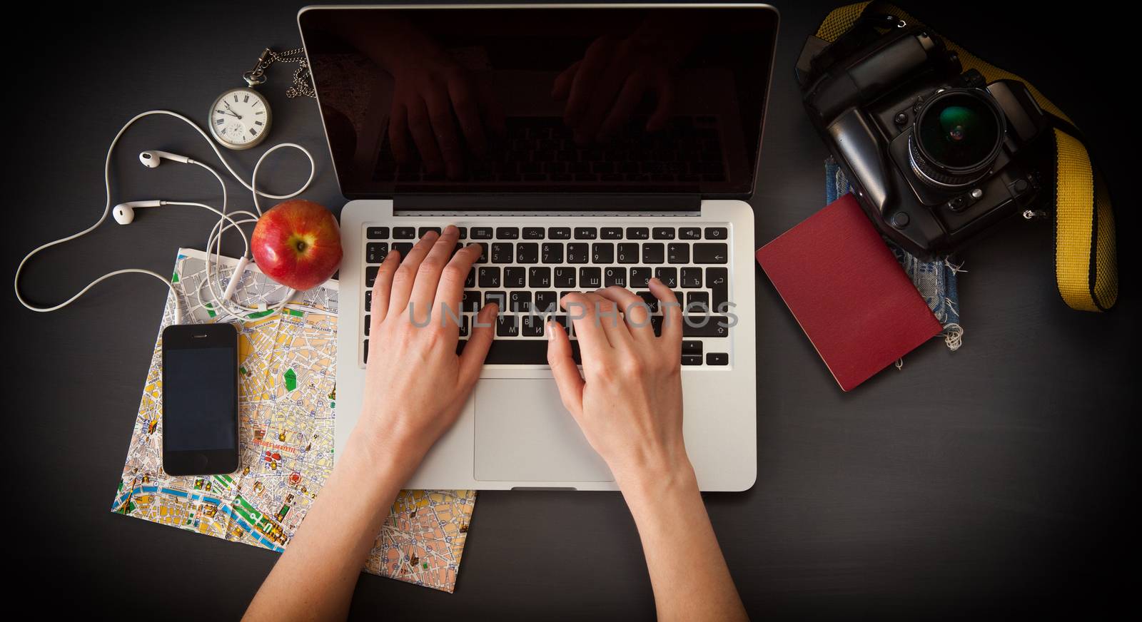 Outfit of the traveler. The view from the top. young woman sitting at the vintage brown wooden table. there are the map, camera, passport, watch, laptop and mobile phone with headphones on the table 