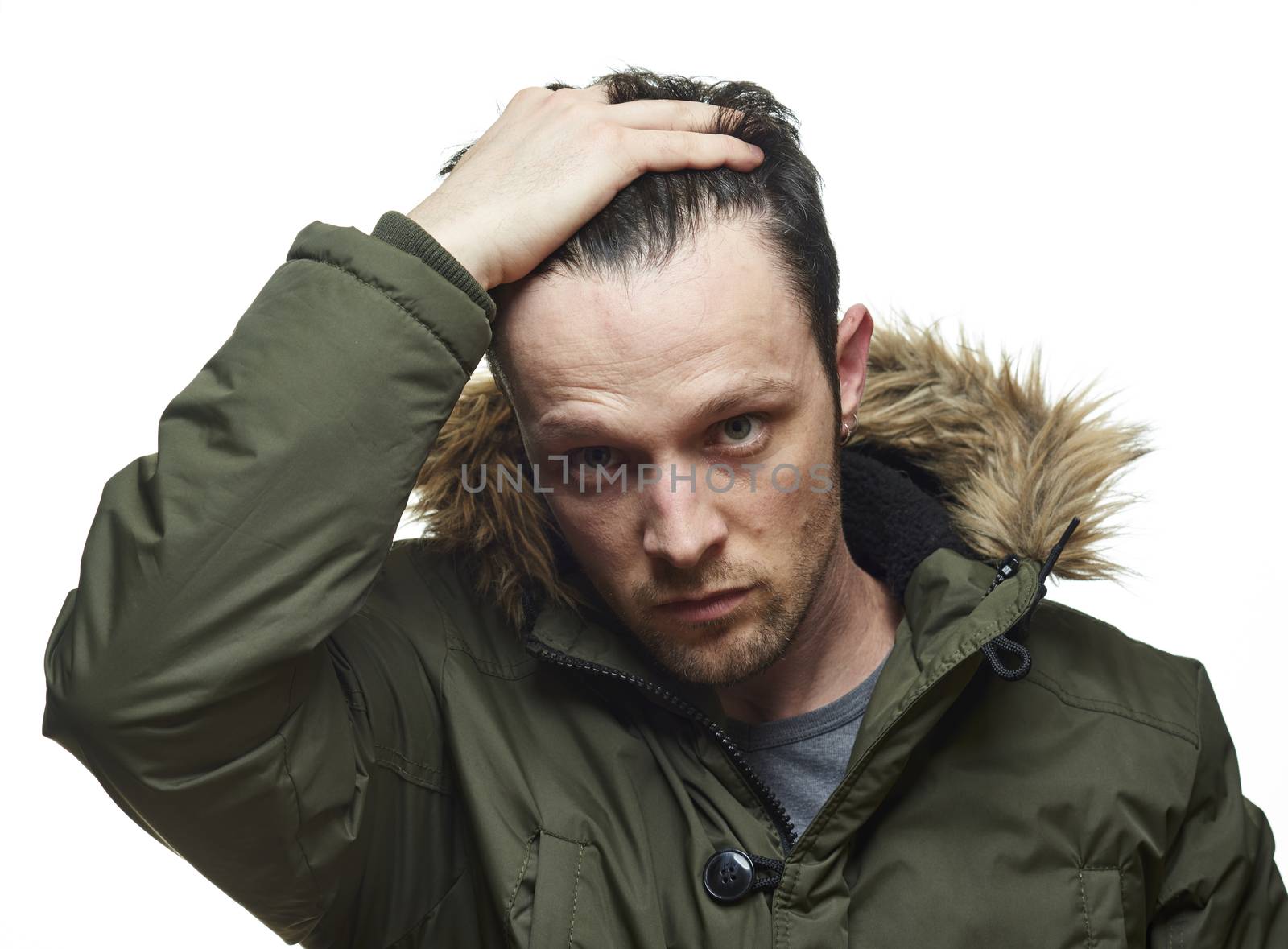 High key studio portrait of young adult caucasian model wearing hooded winter coat running fingers through his hair.